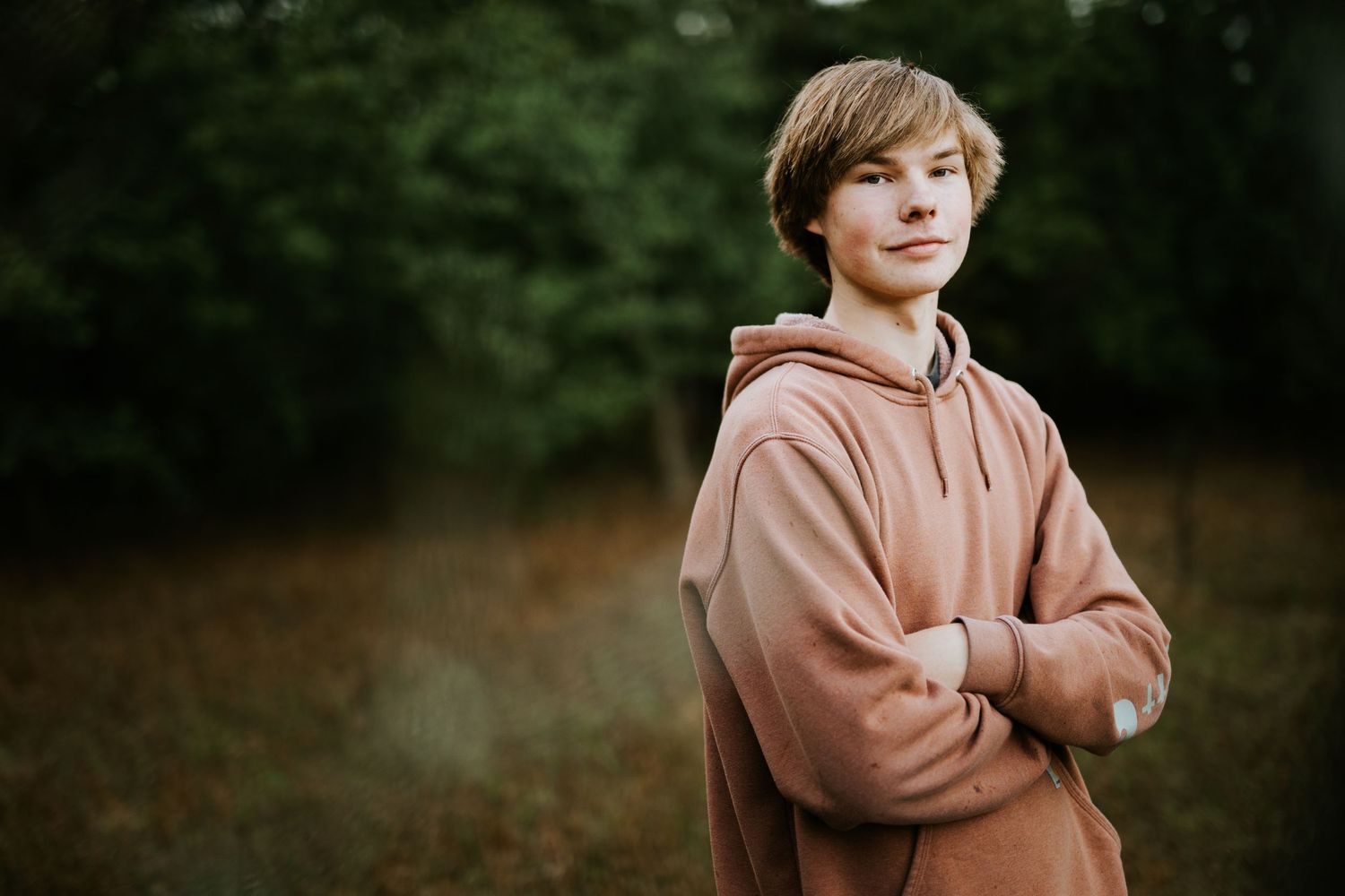 Youth in casual brown hoodie posing outdoors in natural setting.