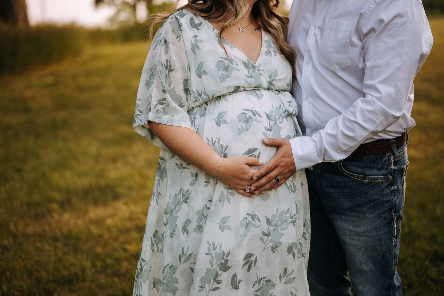 Maternity portrait of couple in casual attire outdoors at golden hour.