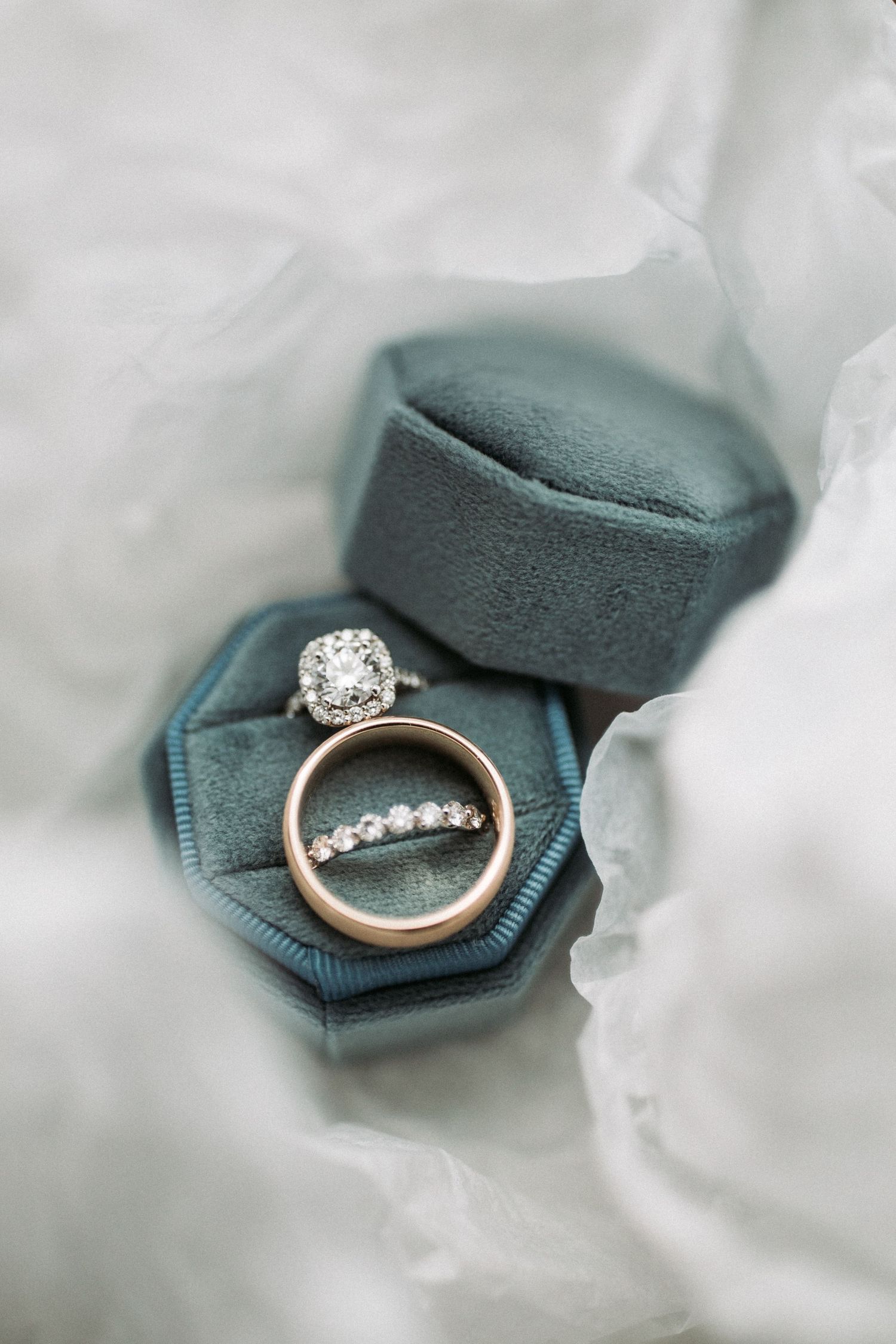 Diamond engagement ring nestled in a teal velvet ring box surrounded by soft white fabric.