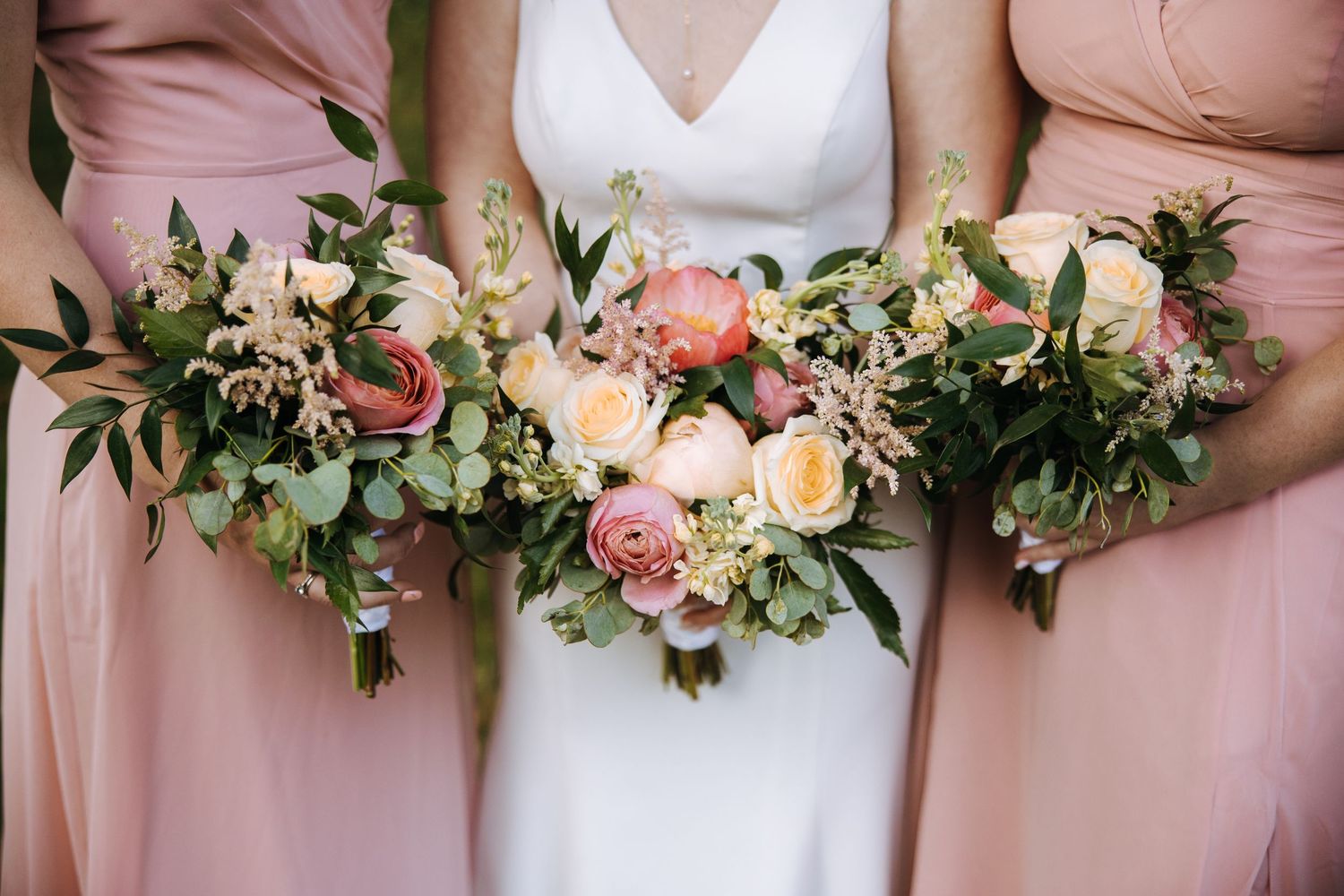 Row of pink and white floral bouquets held against blush pink bridesmaid dresses.