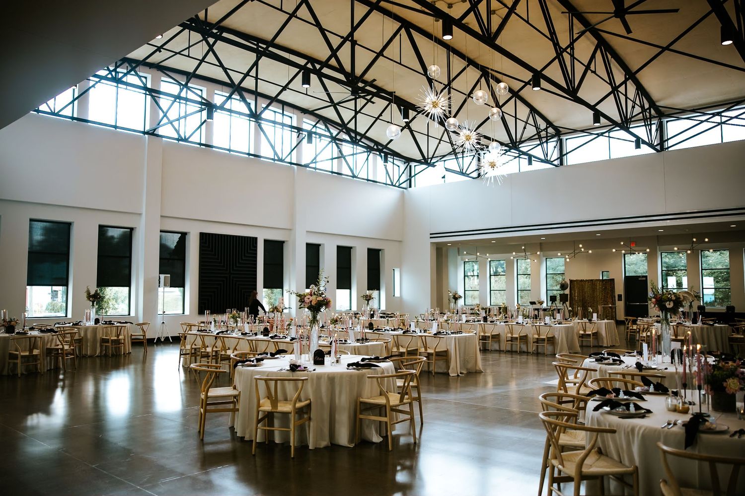Large elegant wedding reception venue with white tables and chairs set up under industrial skylights.