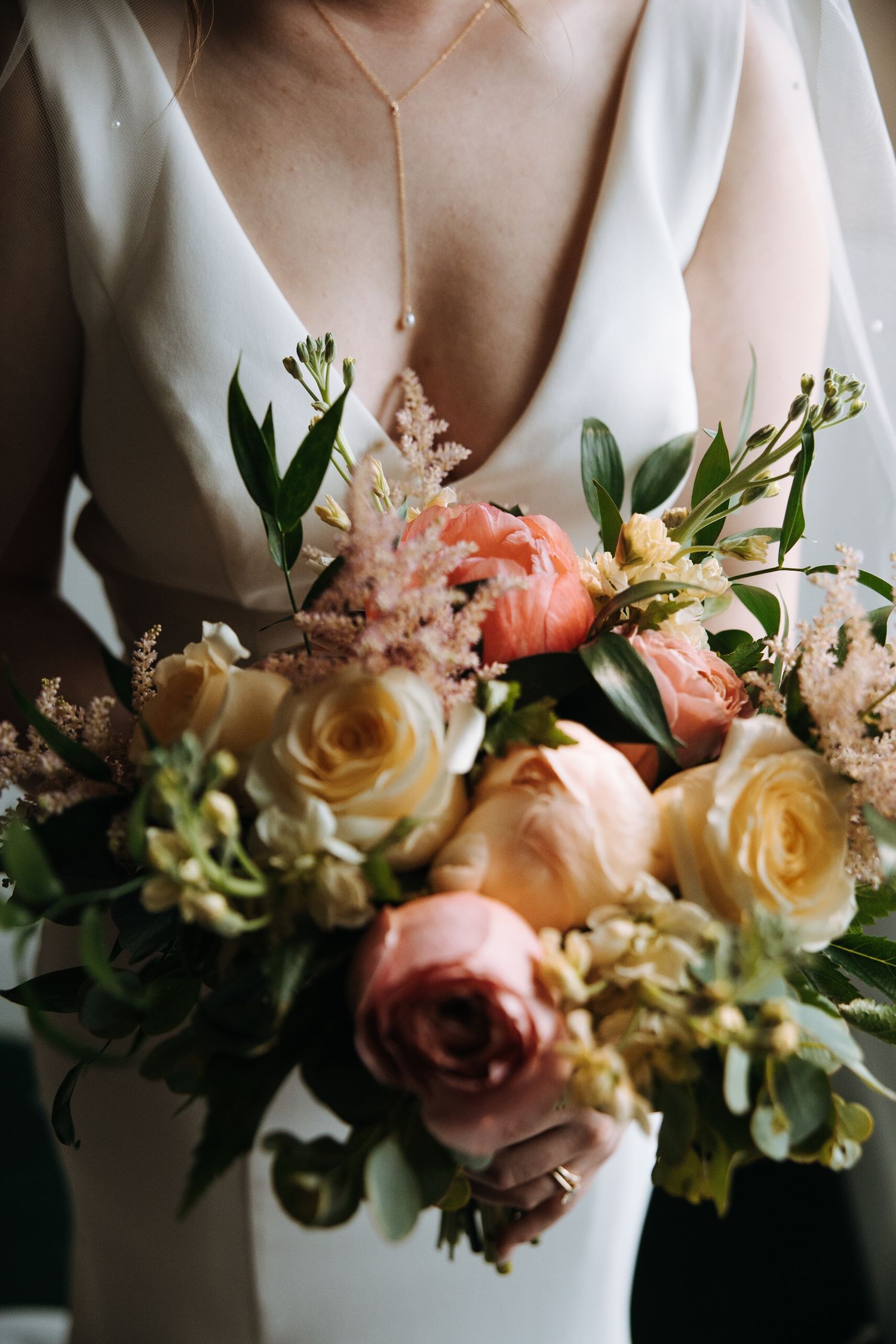 An elegant bridal bouquet with peach and cream roses against a white wedding dress.