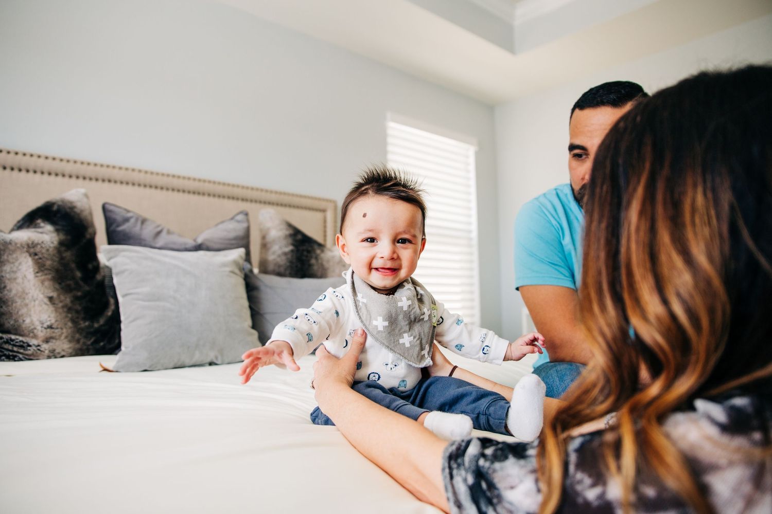 a baby boy smiles at the camera while his parents talk to him