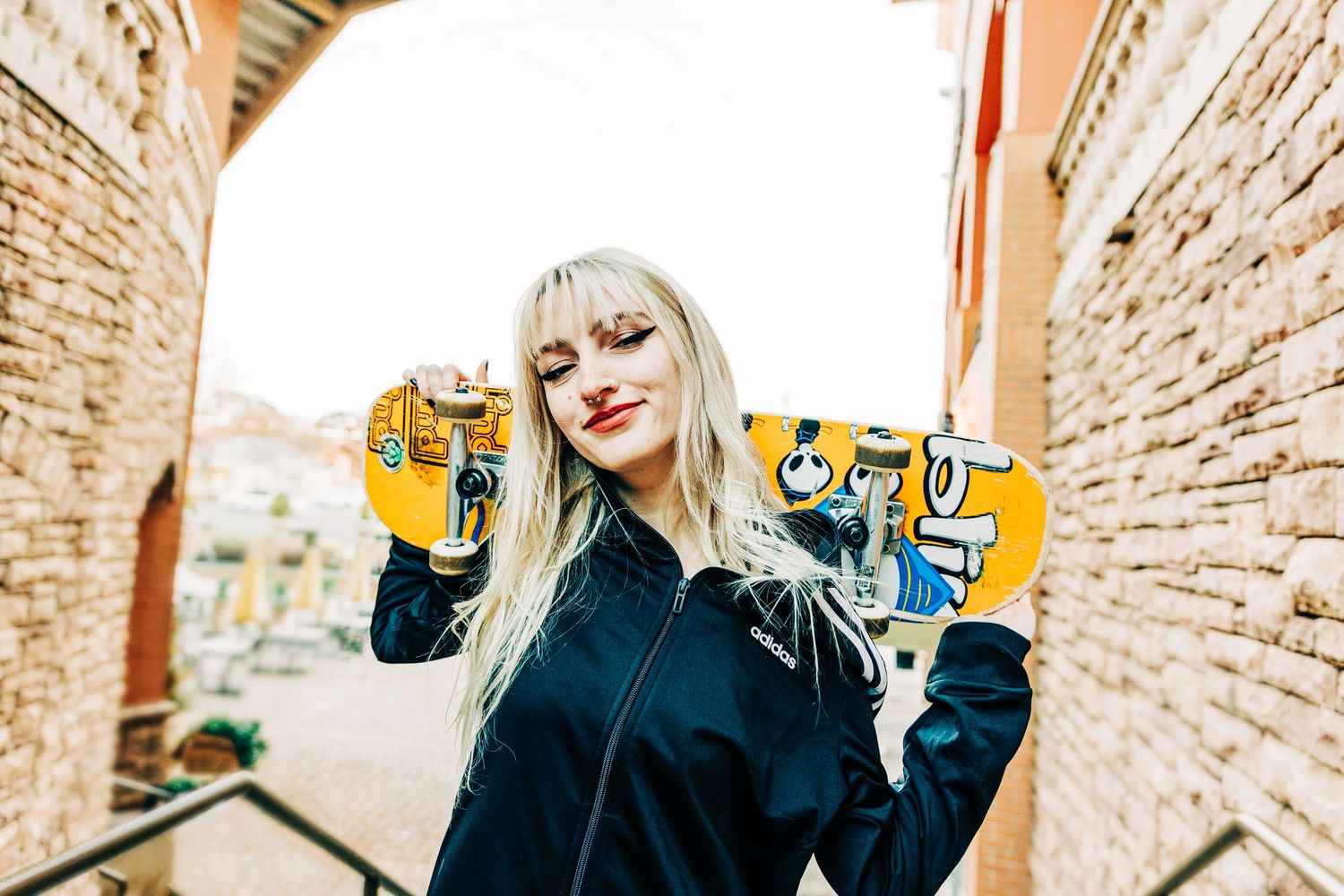 Person in black jacket holding up yellow skateboard between brick walls on sunny day for Charlotte Senior Photographer