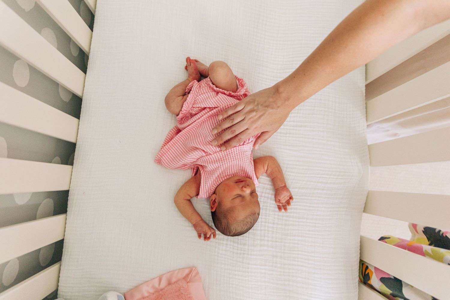 A mother's hand gently draped across a newborn who lies sleeping in her crib during Charlotte newborn photography session.