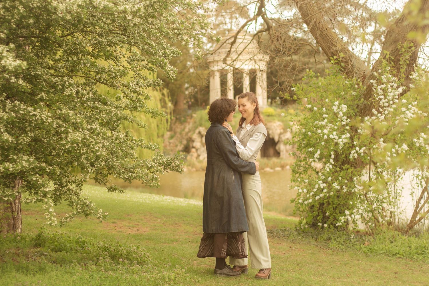 A lesbian couple are standing near to each other, they have their arms around each other. In the background there is a temple.