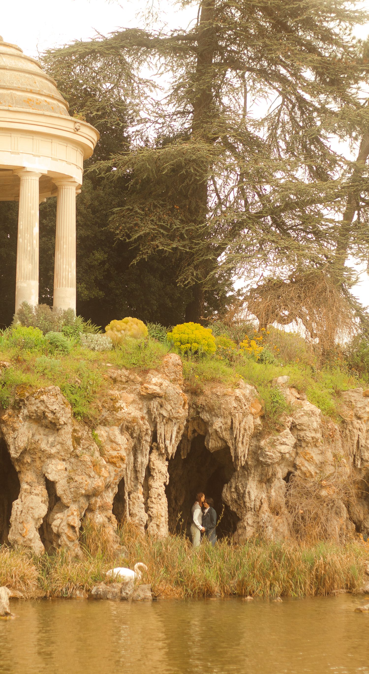A couple is seen standing near to each other inside a a cave, near there is a swan and a temple.