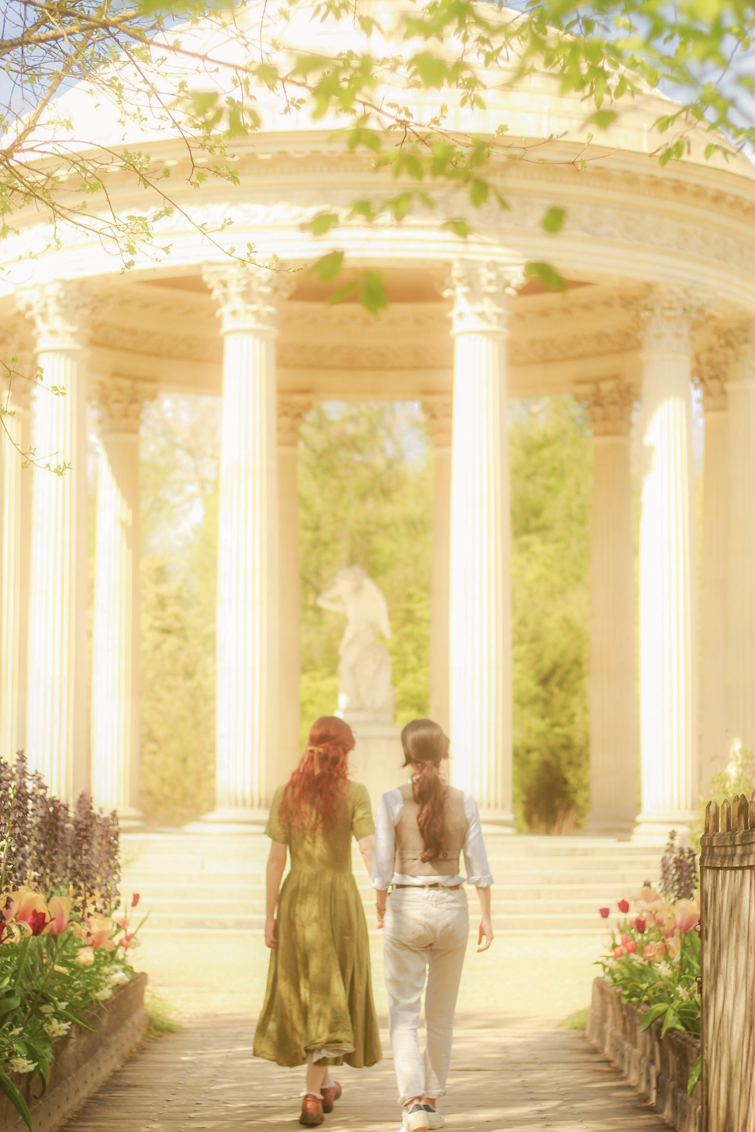 A couple is walking hand in hand surround by flowers and near a temple.