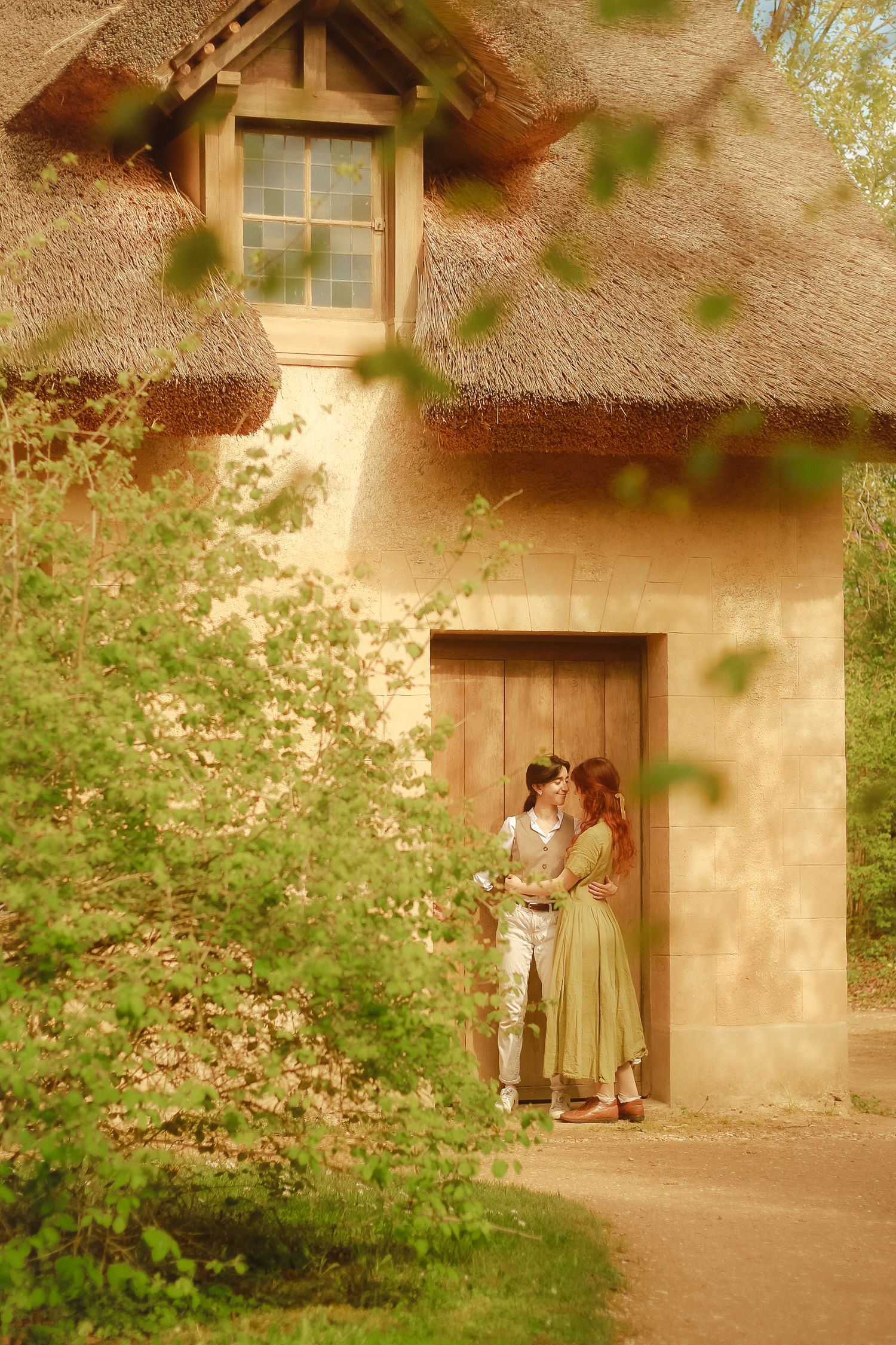 A couple is standing close with their arms around each other, near the door to a cottage.