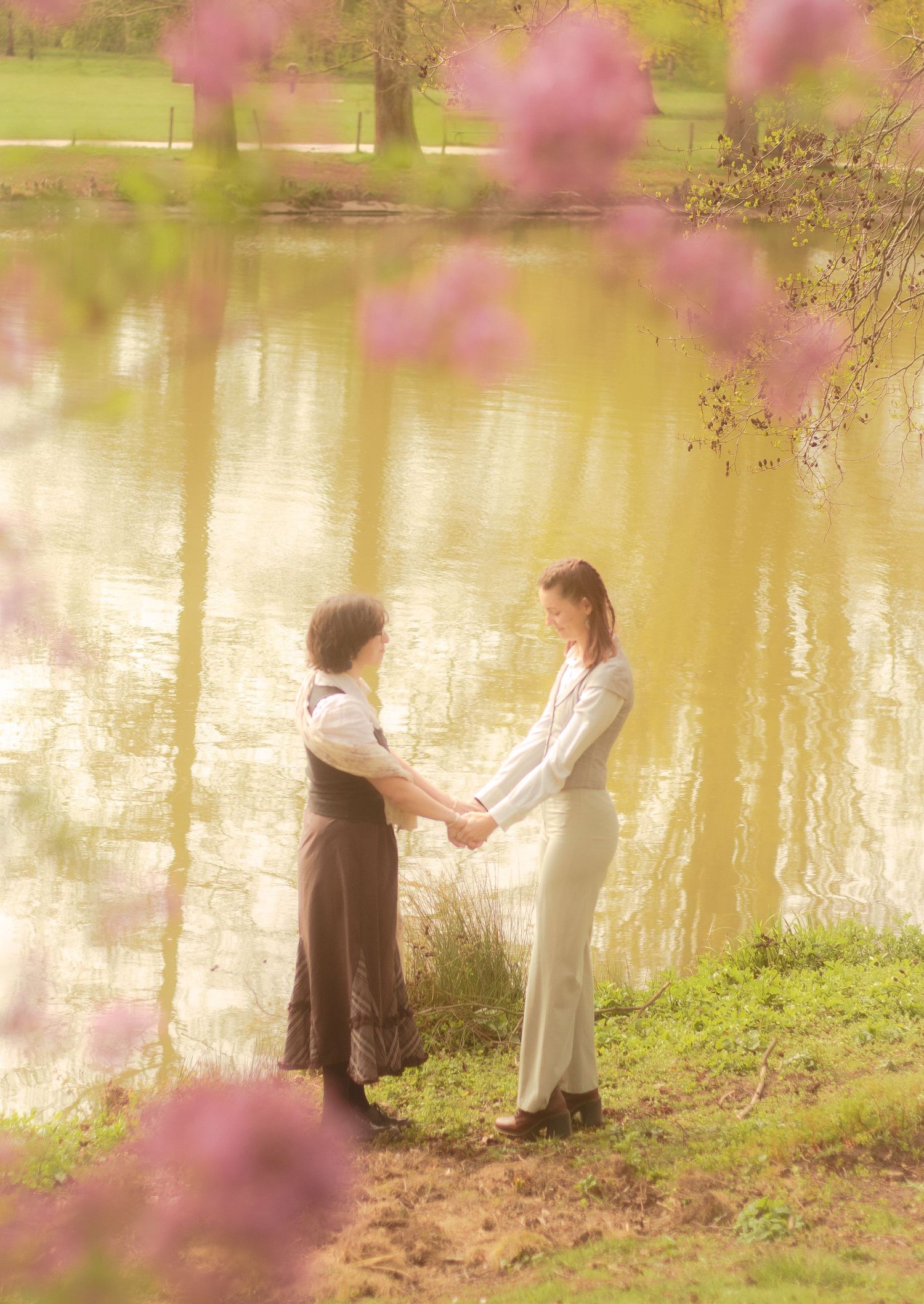 Two girls are holding hands, they're a lesbian couple. In the background there is a calm body of water.