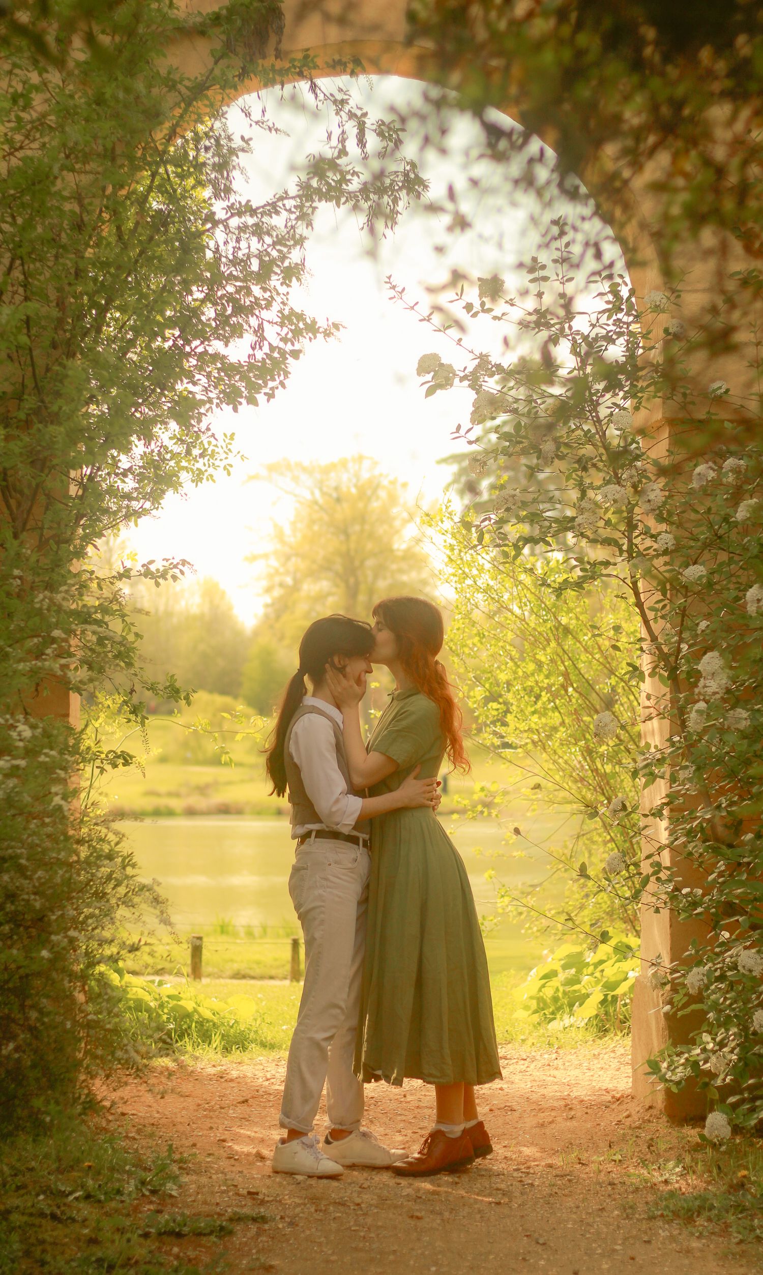 A couple is standing close, the girl is kissing the forehead of her lover, they have their arms around each other