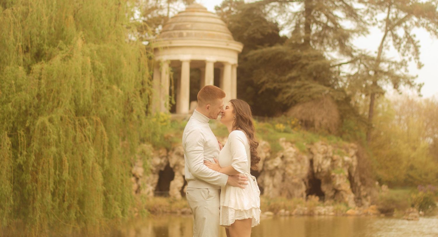 A couple is about to kiss, in the background there is a willow tree and a temple located in Bois de Vincennes.