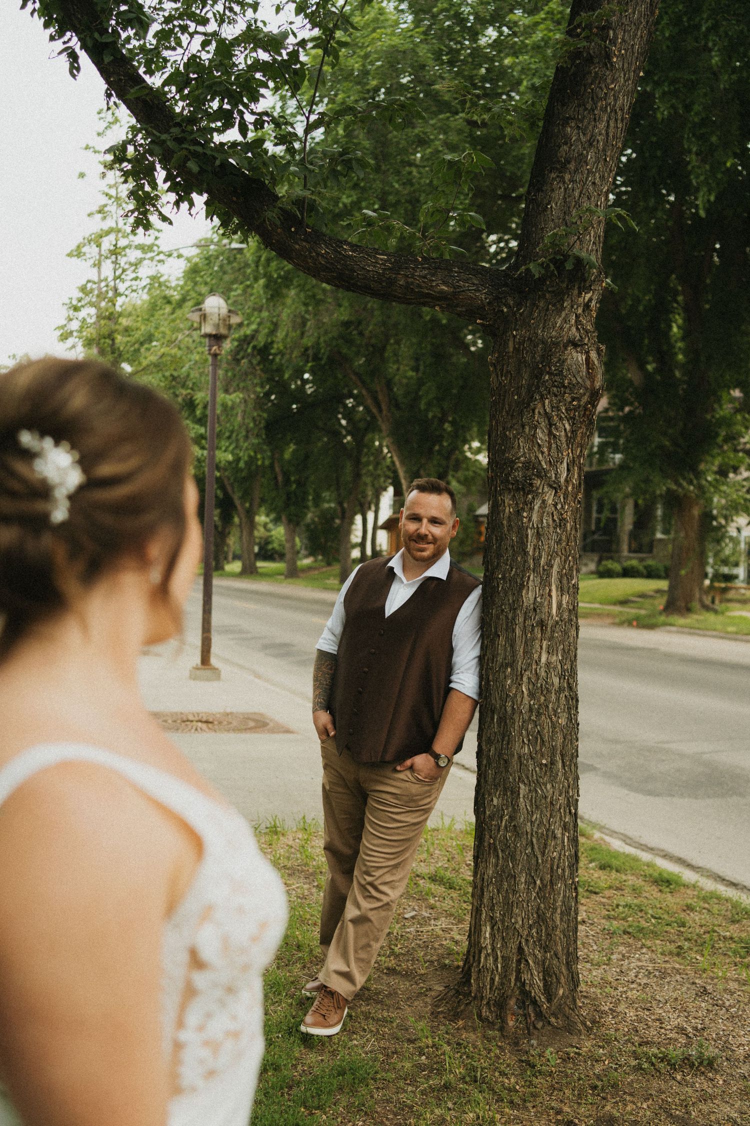 A bride looks at her groom as he leans against a tree