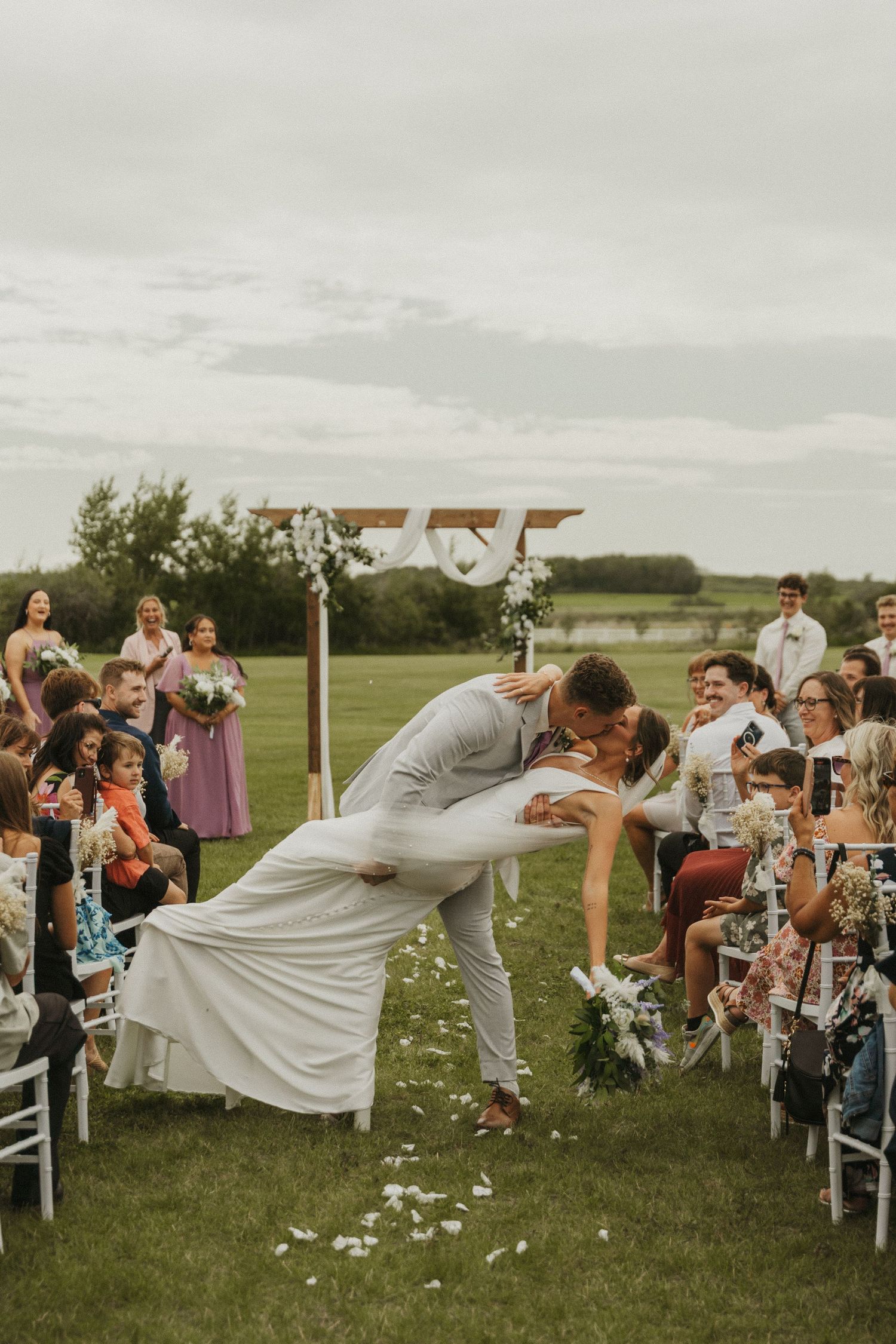 A photo of a bride and groom sharing a dip kiss as they walk down the aisle