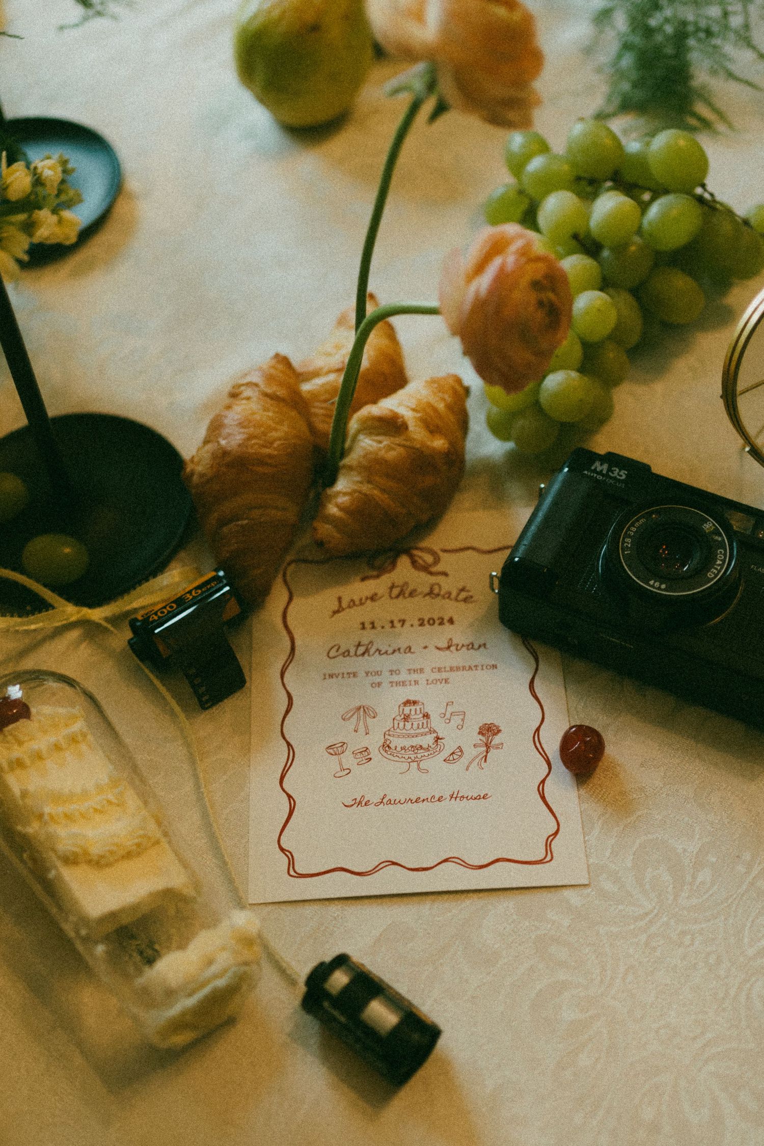 A photo of wedding details including invitations, wedding cake, camera, film and florals.