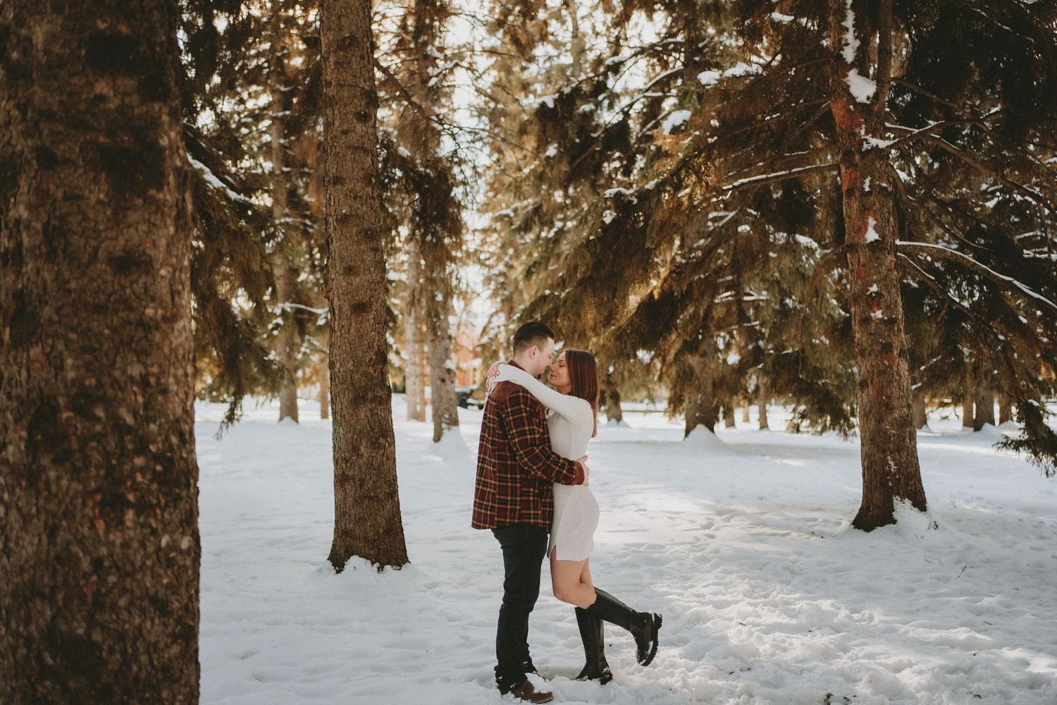 a couple hug in the snow, surrounded by trees