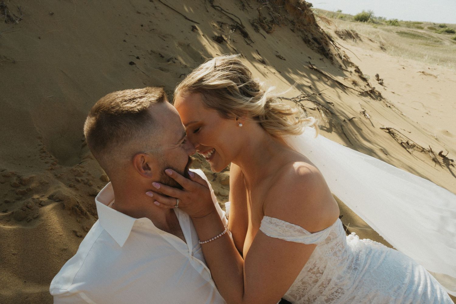 A bride and groom roll around in the sand in the desert