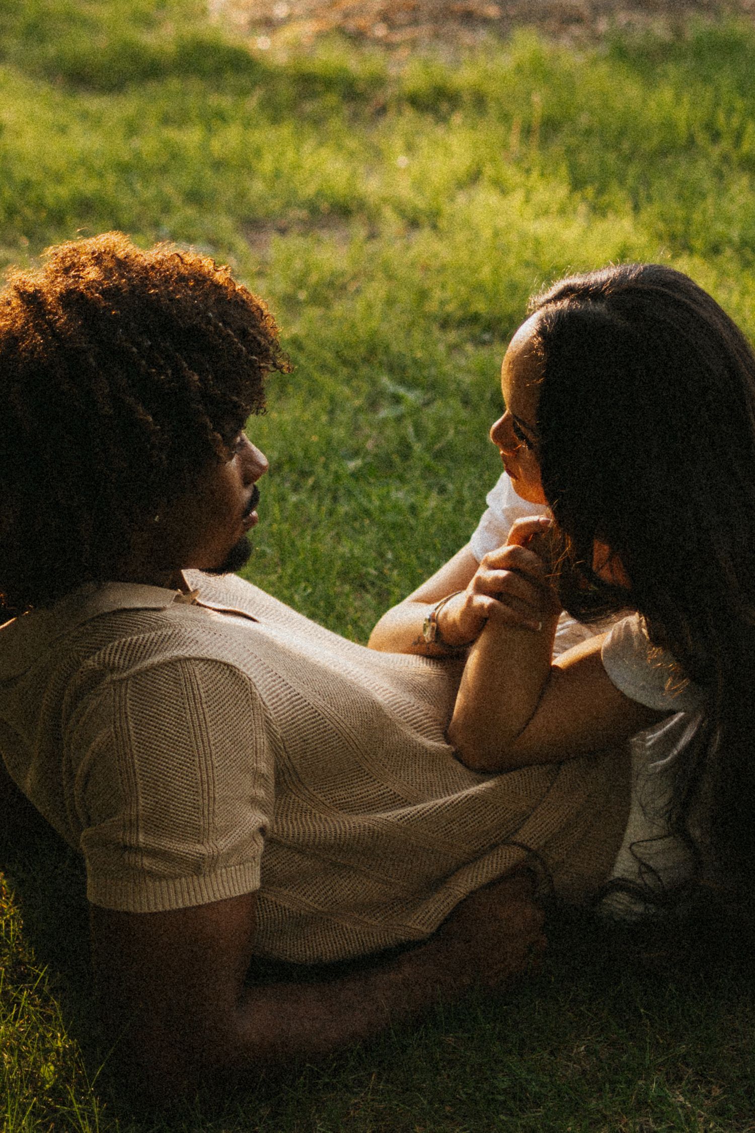 A couple lays in a field at golden hour, looking at each other romantically
