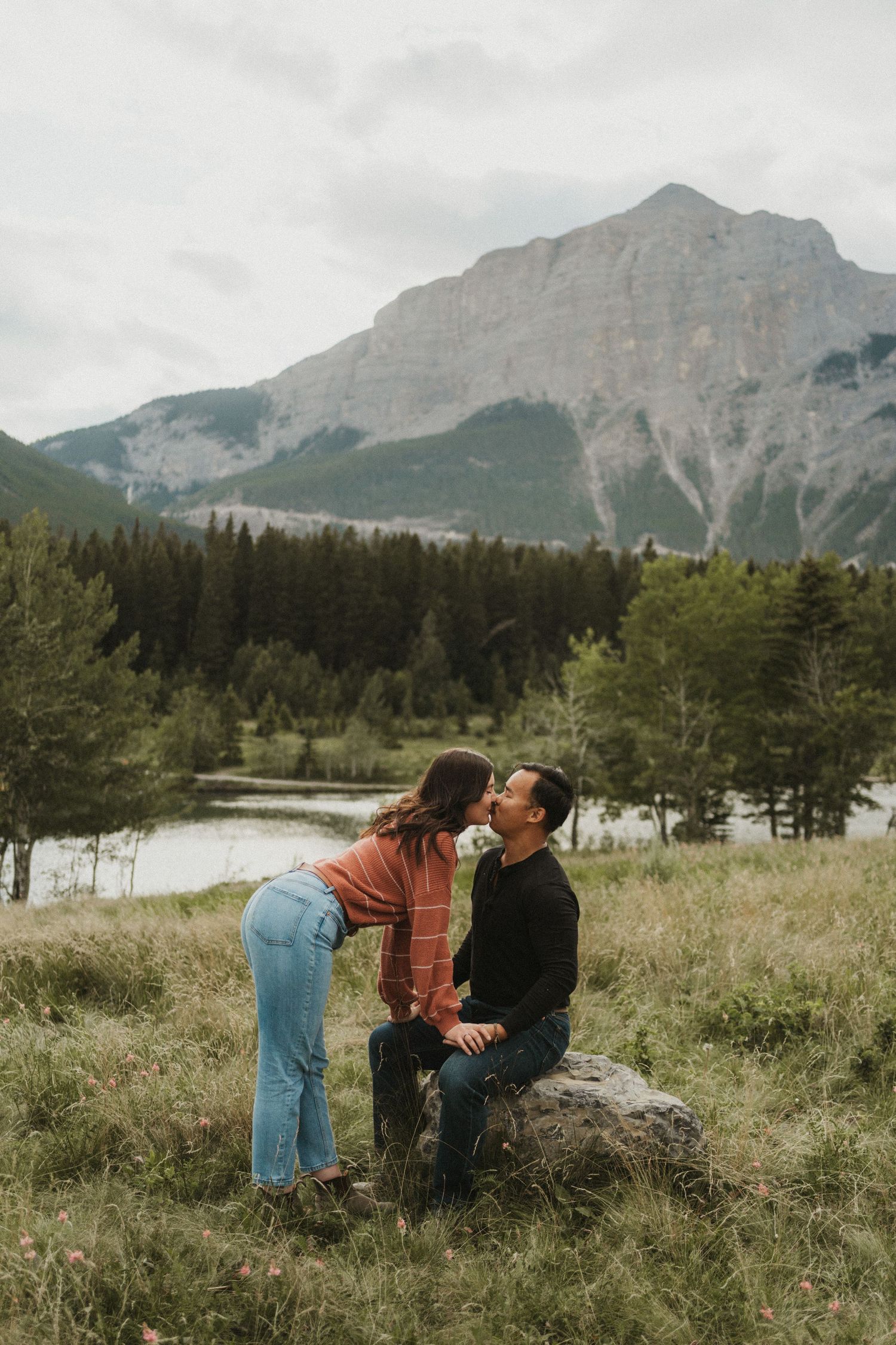 A photo of a woman kissing a man in front of a big mountain in Canmore