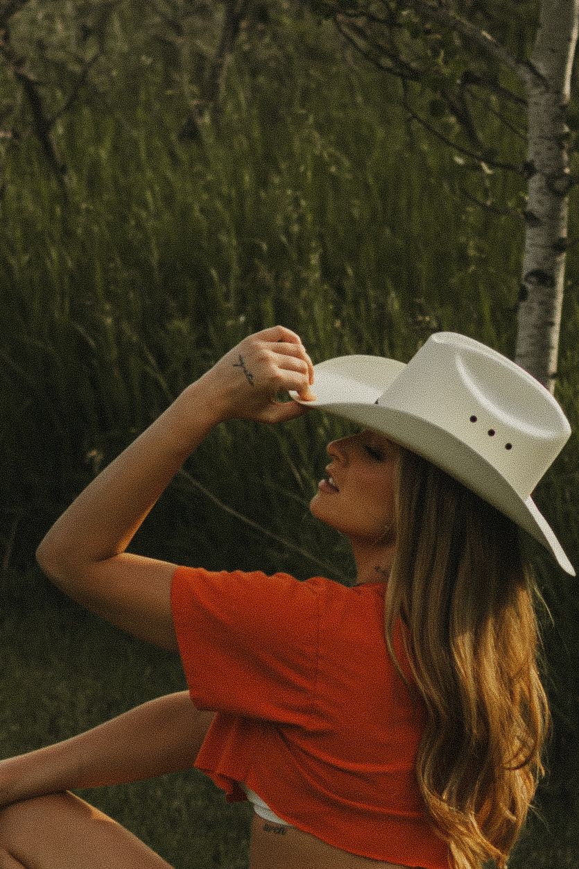 A photo of a woman with a cowboy hat, outside at golden hour.