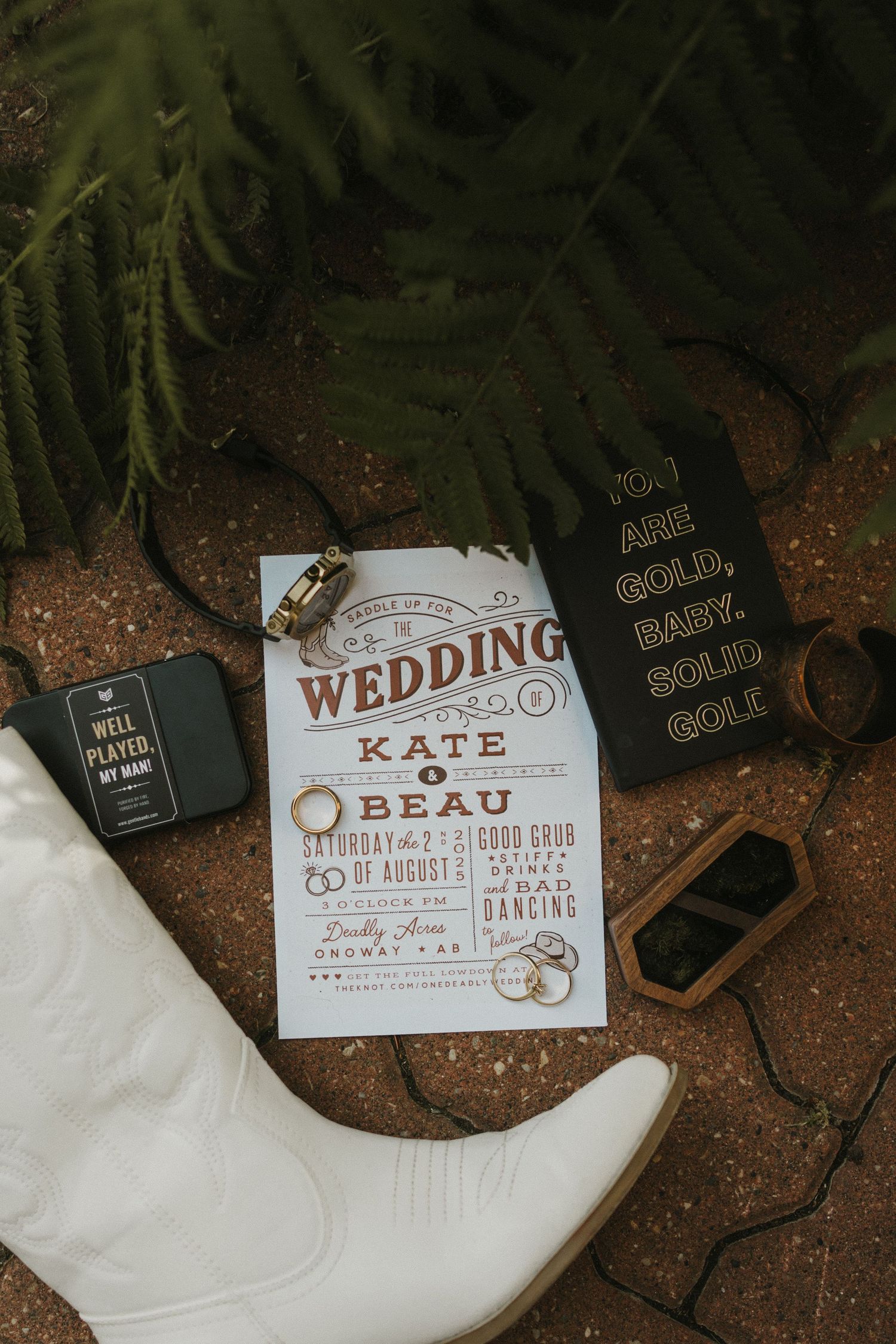 A photo of wedding details. Includes cowboy boots, wedding invitations, wedding rings and nature.