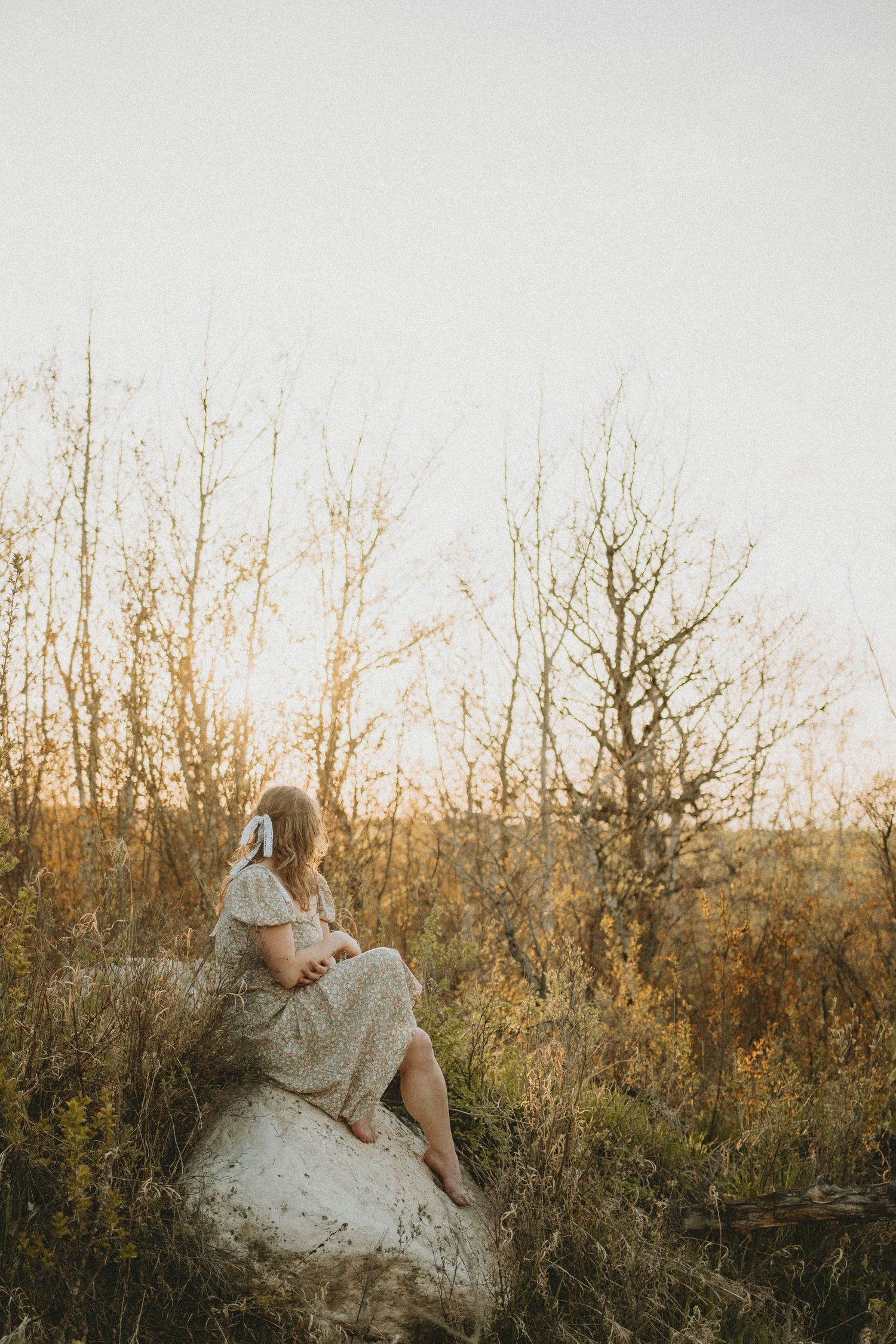 A woman sits on a rock and looks at the sunset