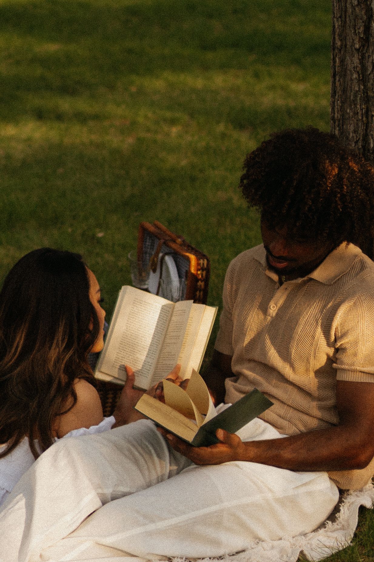 A couple reads books in the park at golden hour.