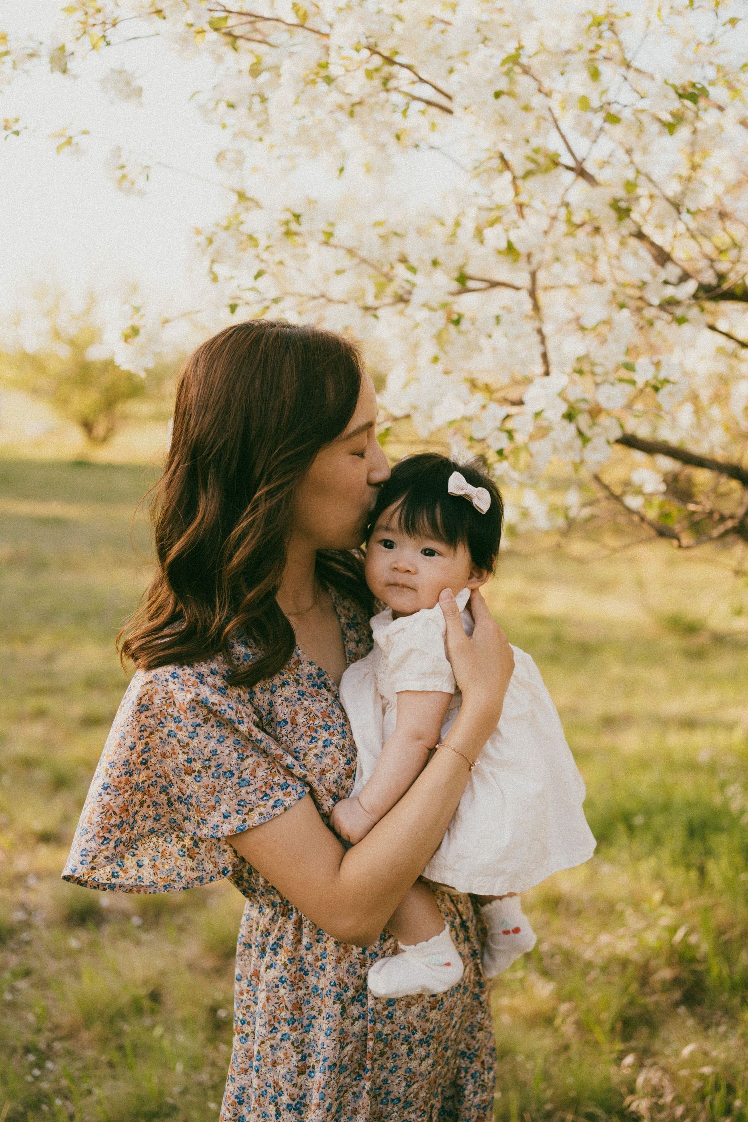 a mother kisses her baby in the blossoms