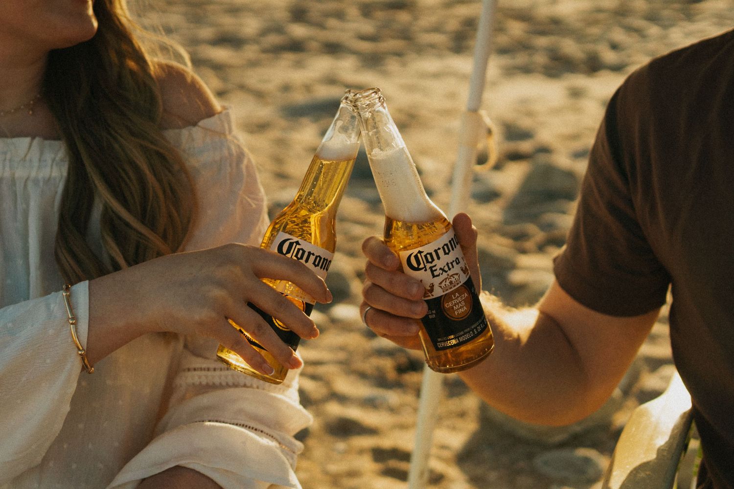 A photo of a couple on the beach, drinking beer.