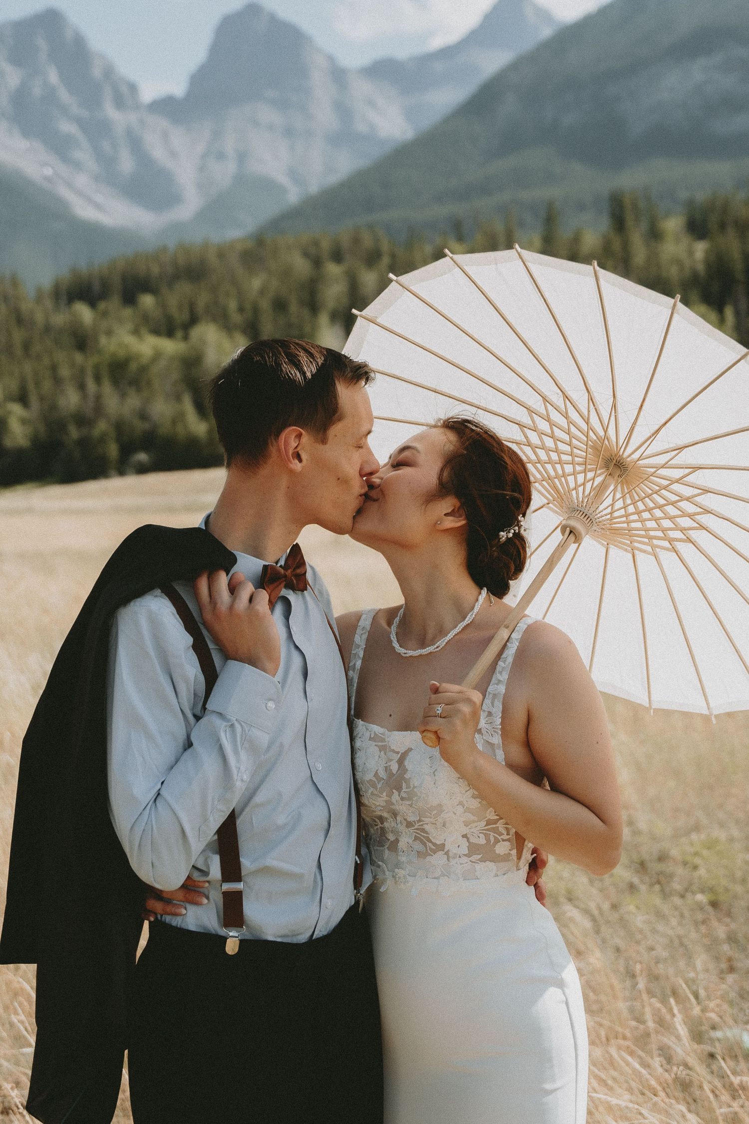 A couple shares a kiss in the Canadian Rockies after they eloped. The woman carries a parasoul.