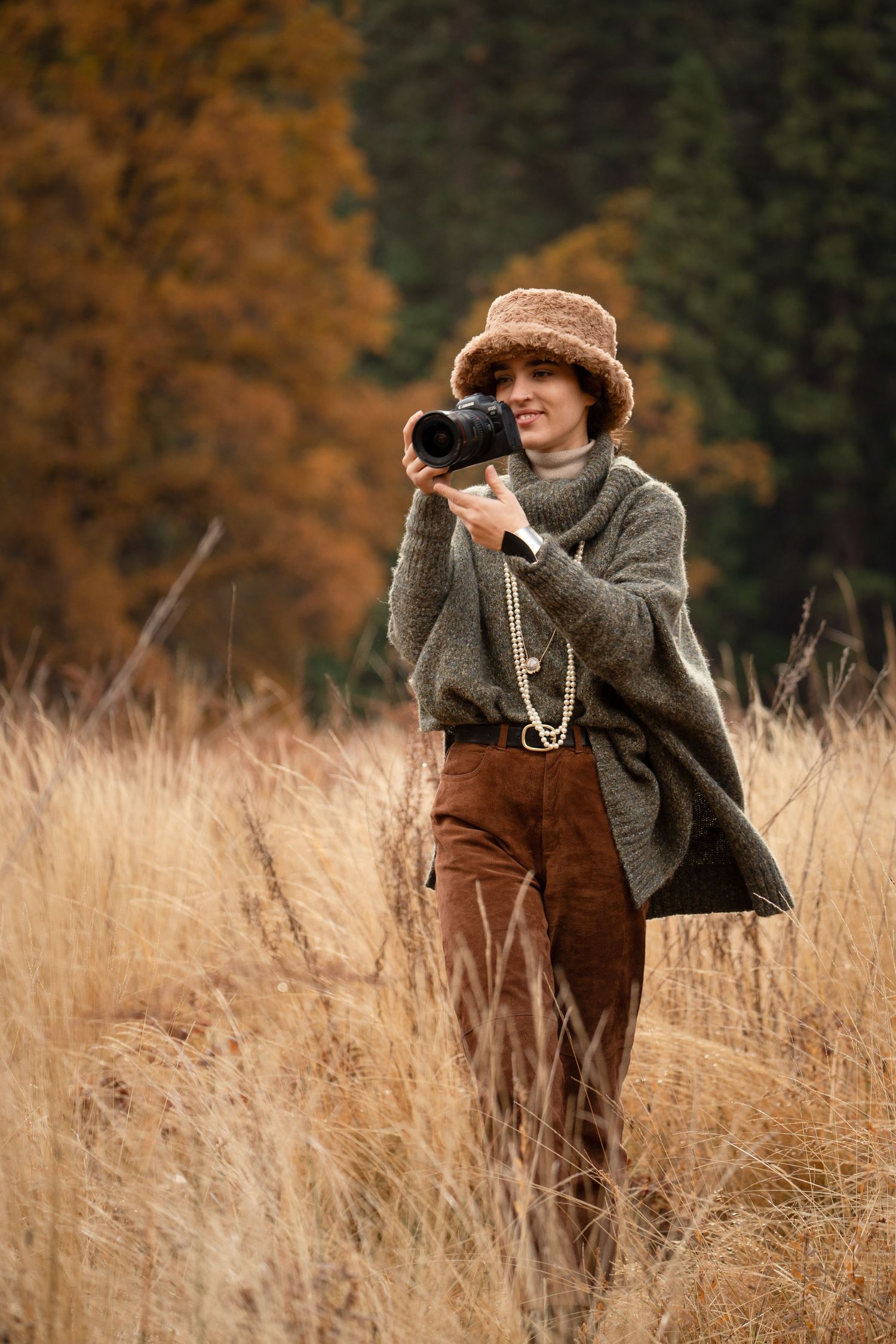 Photographer in tweed coat takes pictures in tall autumn grass field with golden light and natural scenery.