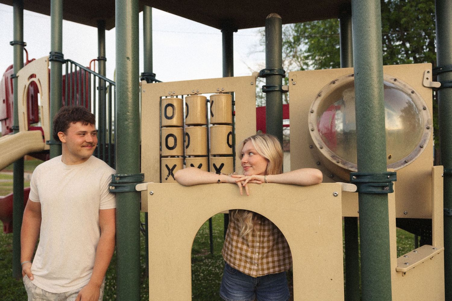 Smiling couple posing playfully at colorful playground structure in park setting.