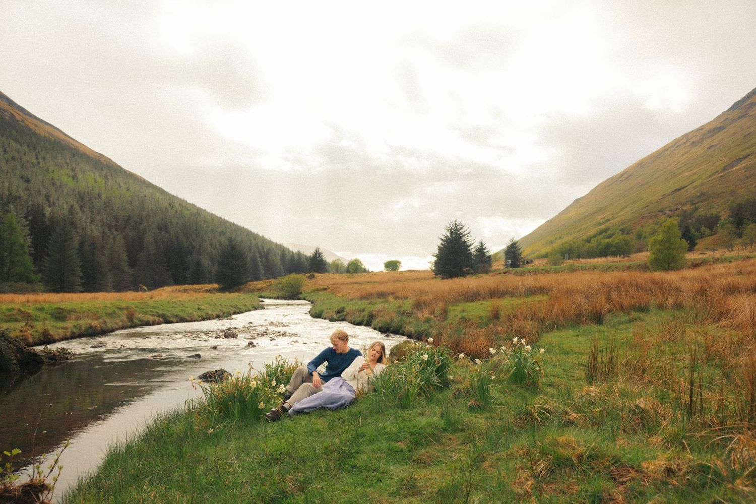 Romantic couple relaxing by a peaceful stream in a scenic highland valley.