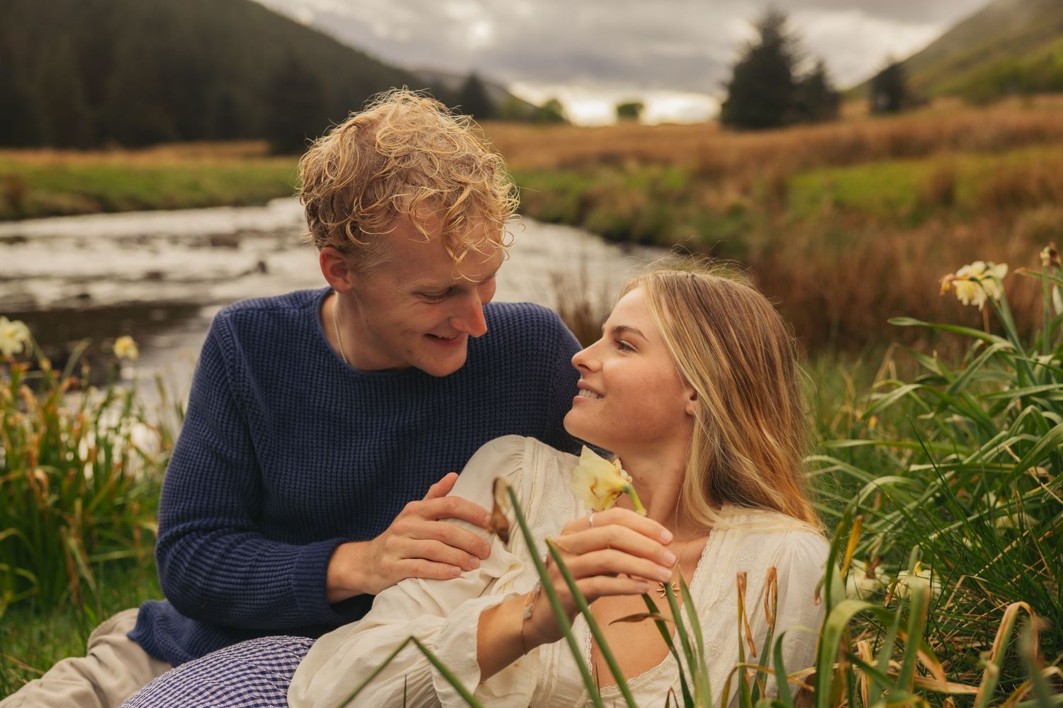 Loving couple sitting together in a lush meadow by a mountain stream.