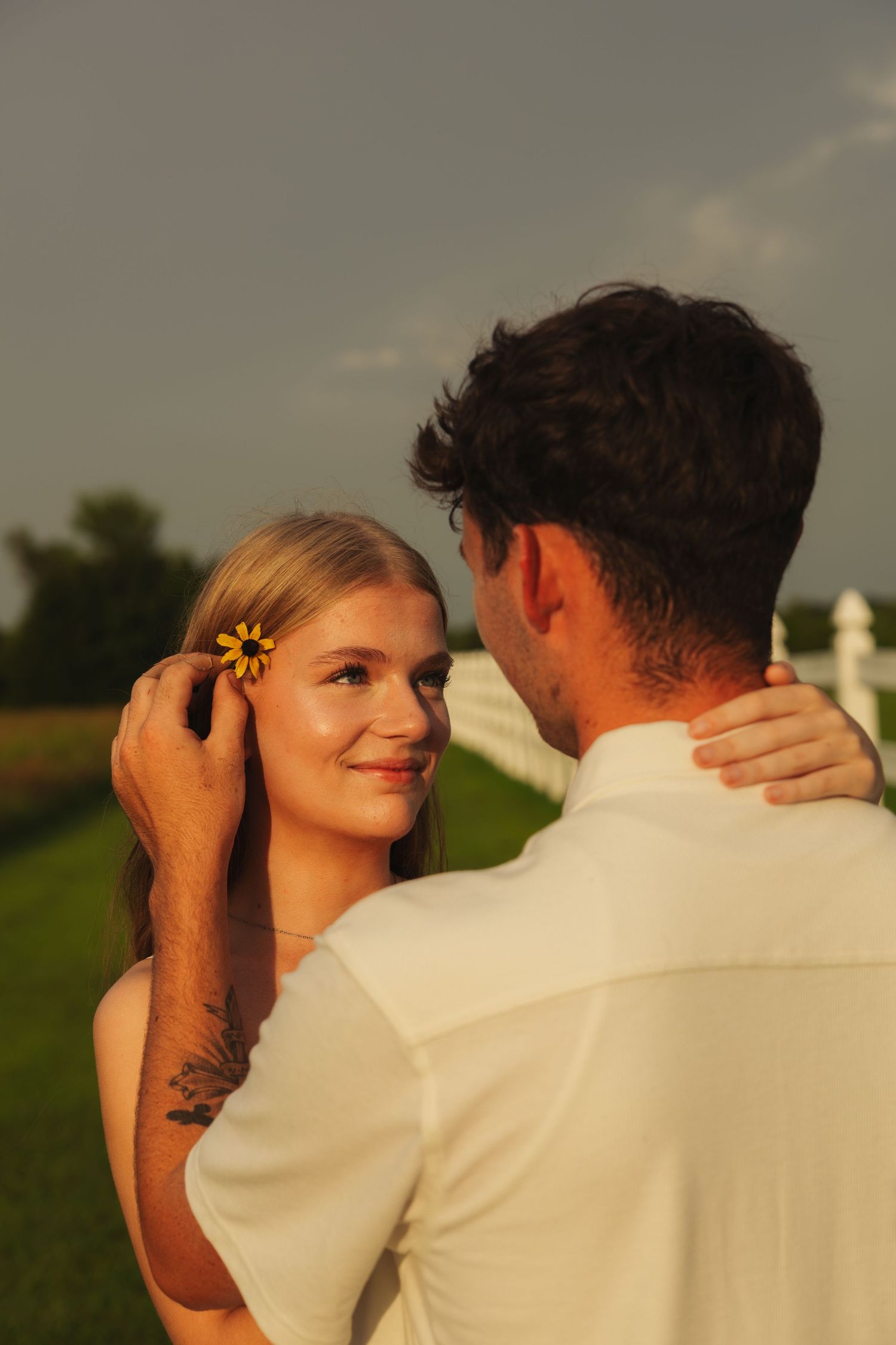 Man placing a yellow flower in a smiling blonde woman's hair at sunset.