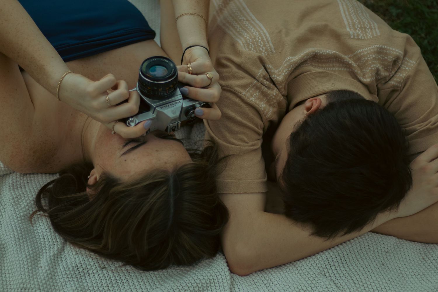 Couple lying down together on a blanket outdoors, woman holding a vintage film camera.