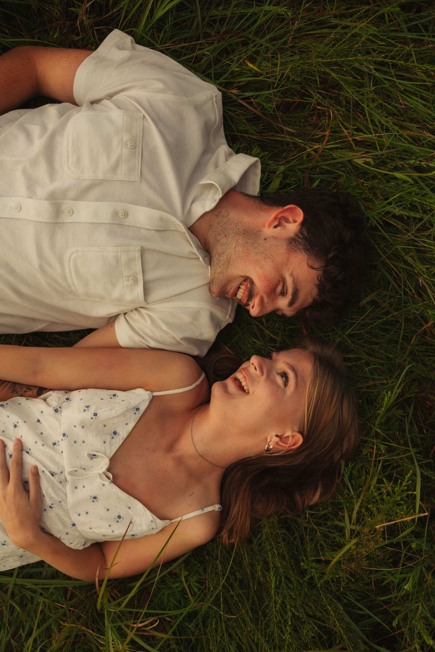 Happy couple lying together in green grass, smiling and looking at each other from above.
