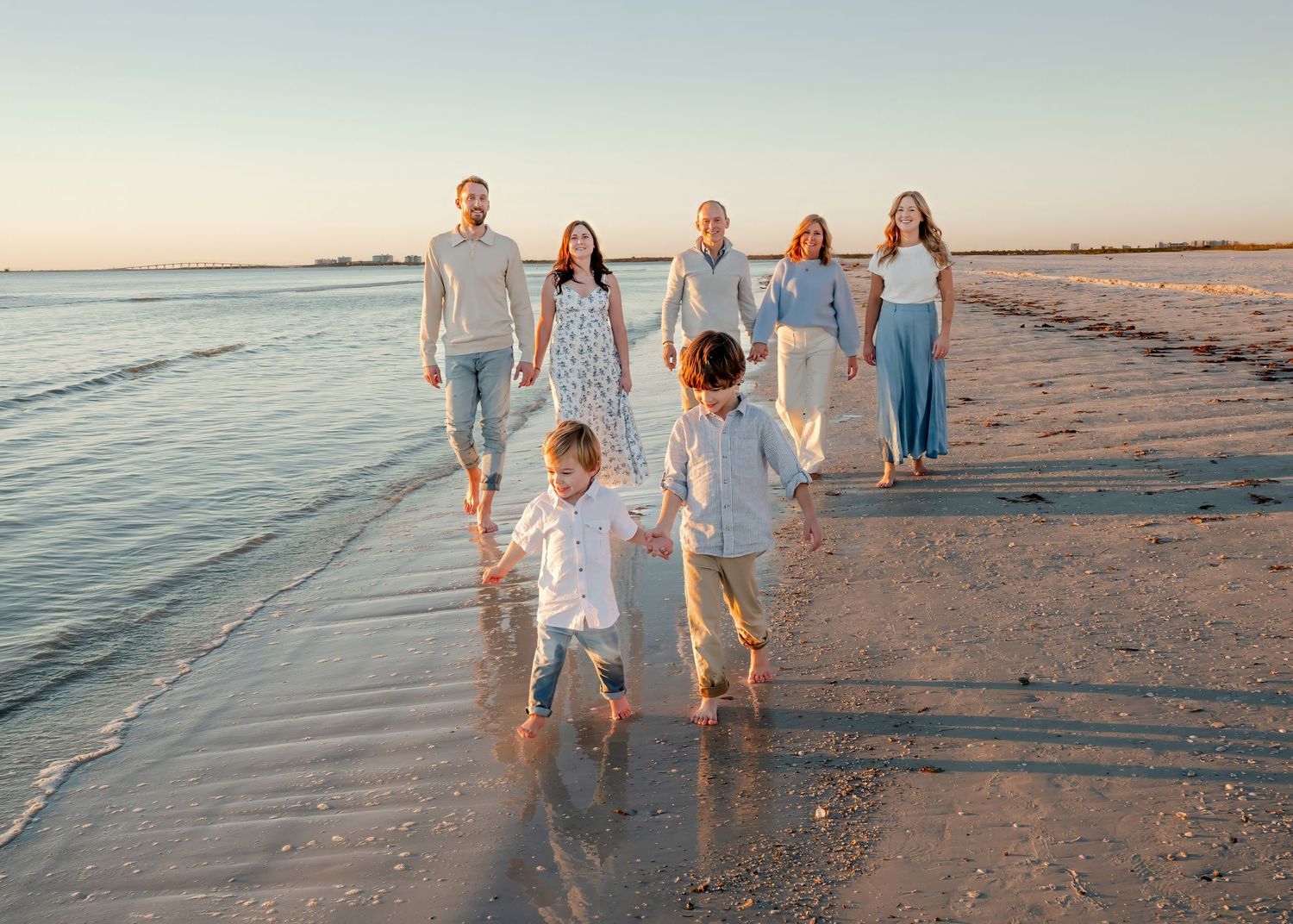 Extended family of seven walking together on sandy beach at sunset.