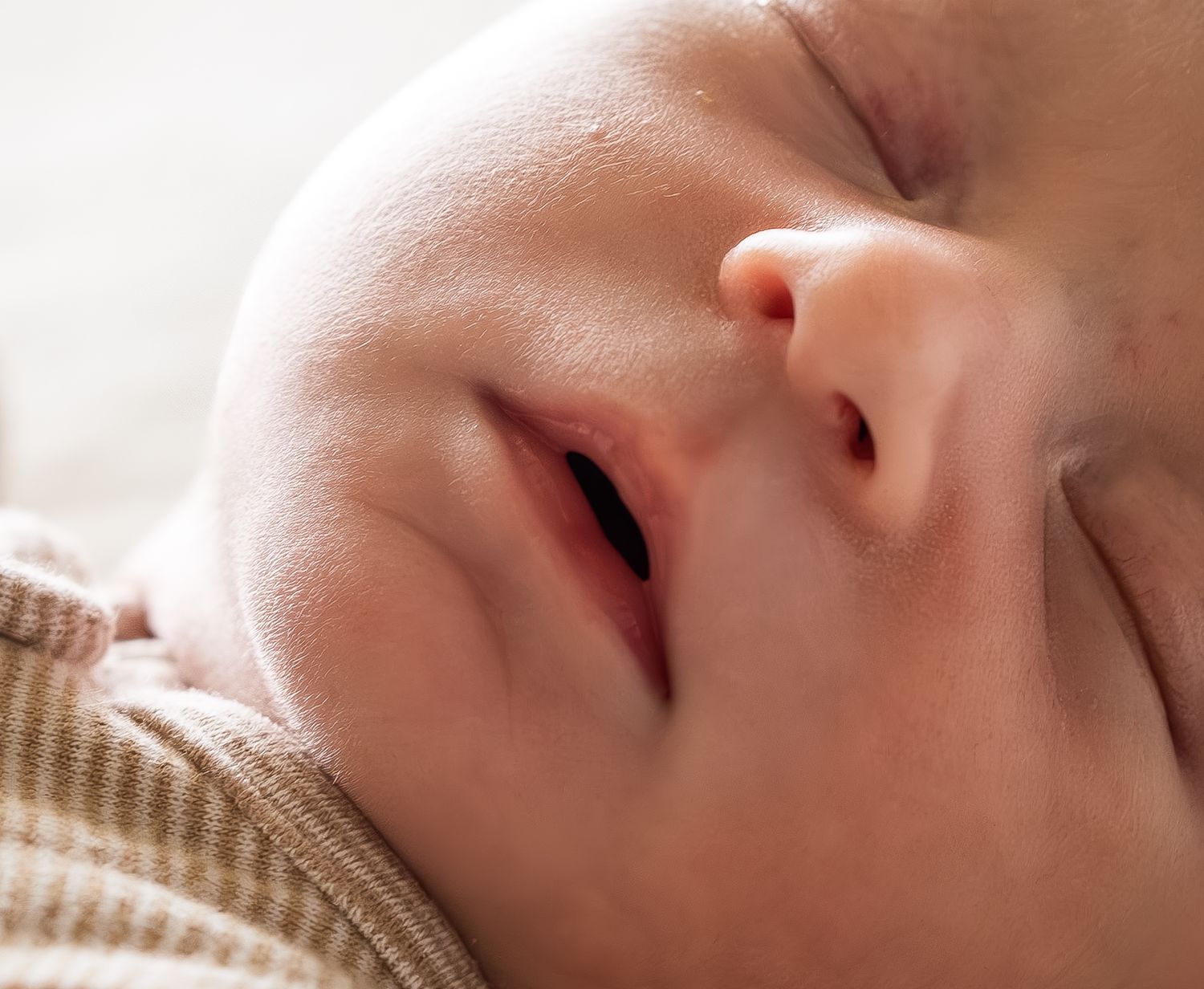 Close-up of a peaceful sleeping newborn baby with soft natural light on face.