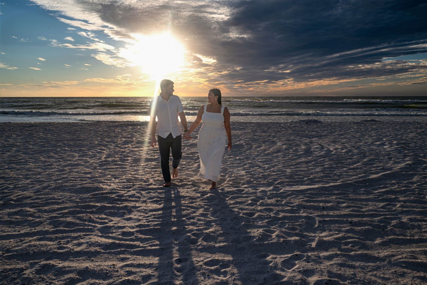 Couple walking hand in hand on beach toward dramatic sunset.