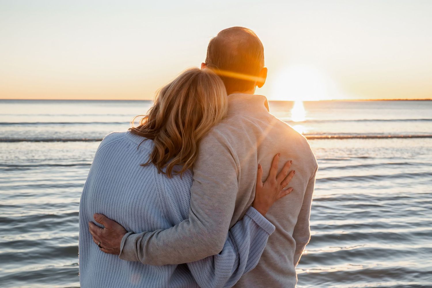 A couple hugging while watching a golden sunset over calm ocean waters.