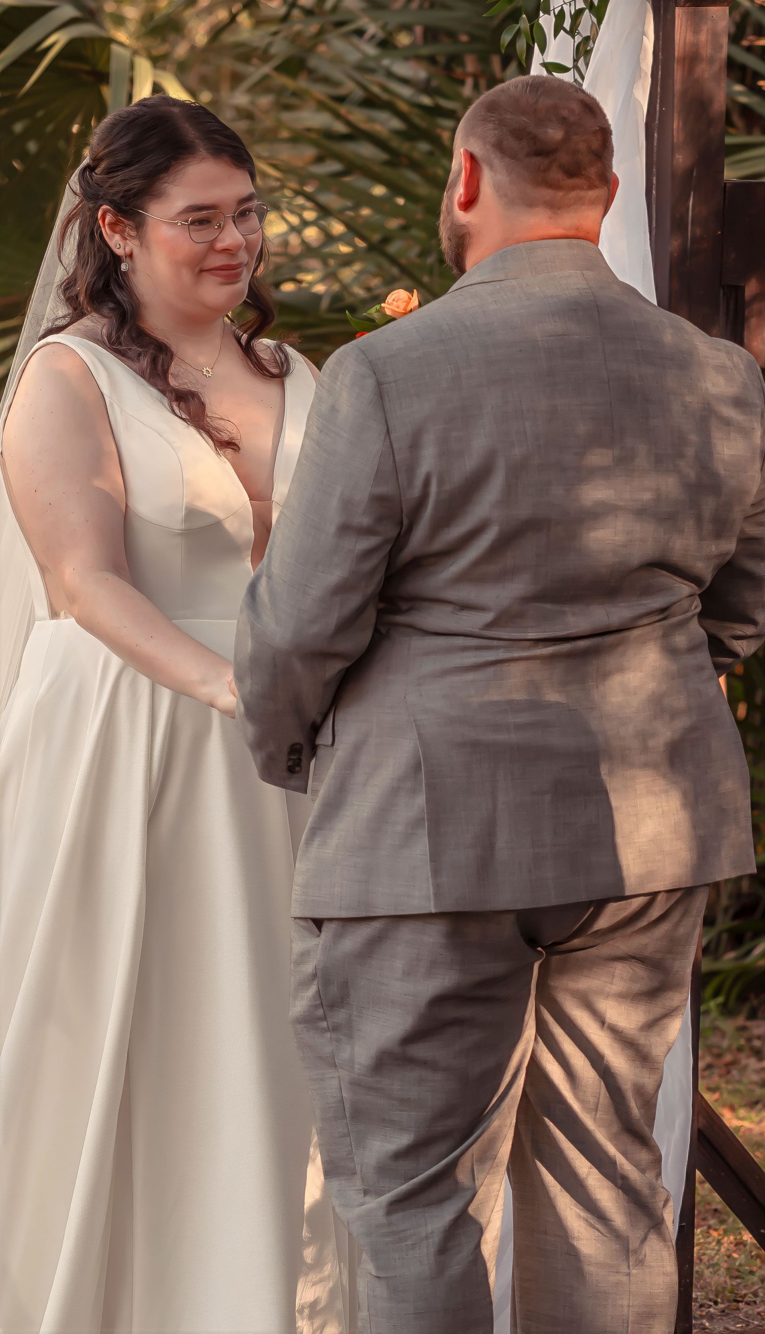 Bride in white gown smiles at groom during outdoor wedding ceremony at sunset.