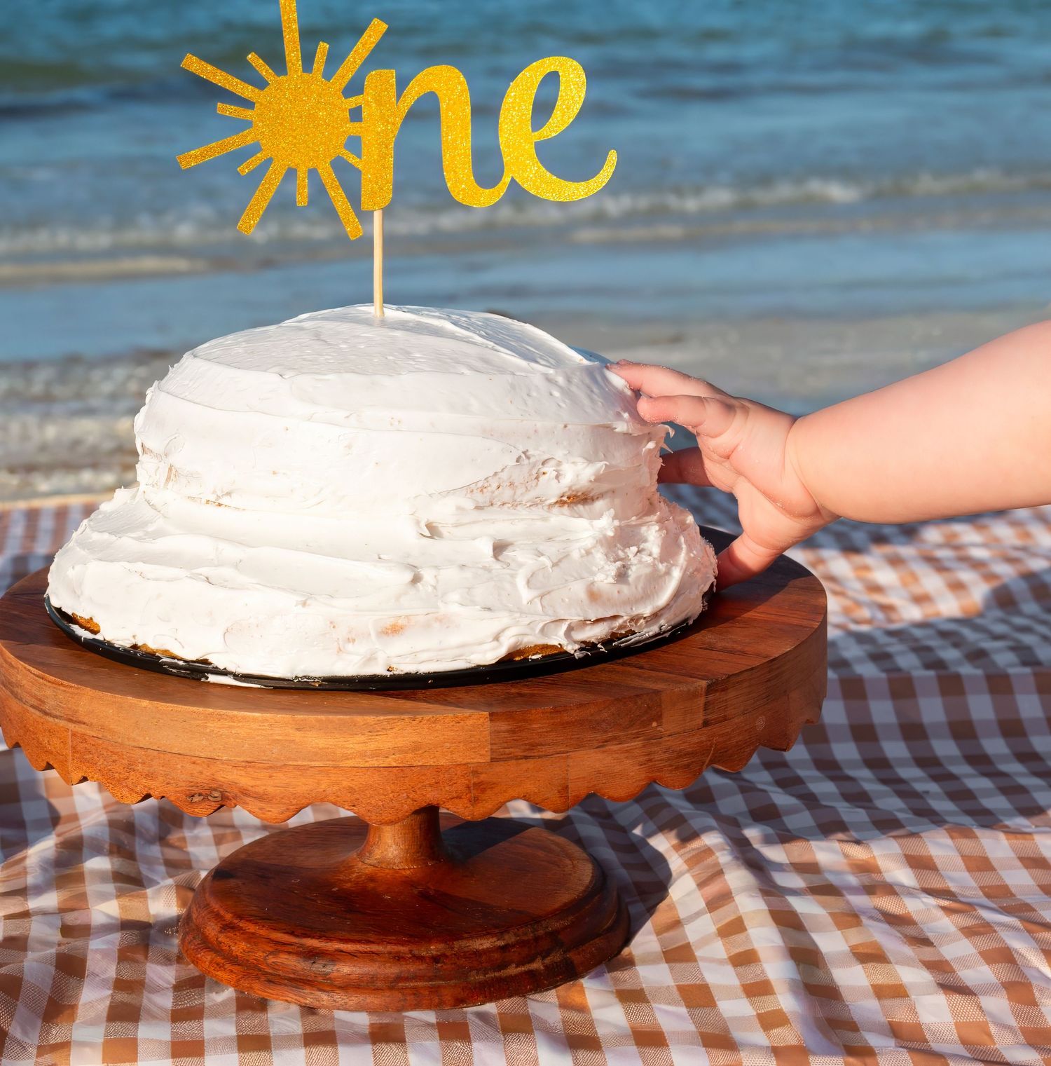 A white frosted first birthday smash cake with a gold 