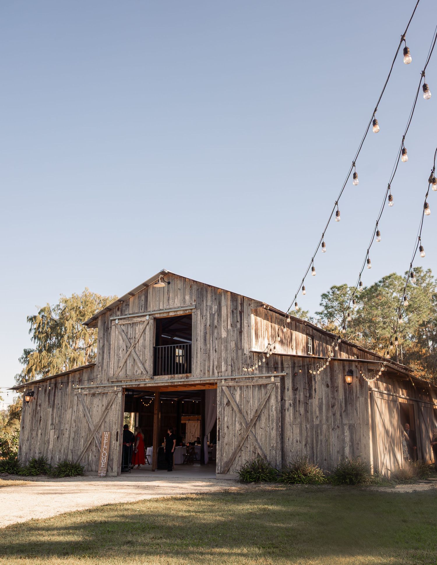 Rustic wooden barn wedding venue exterior with string lights and open doors at golden hour.