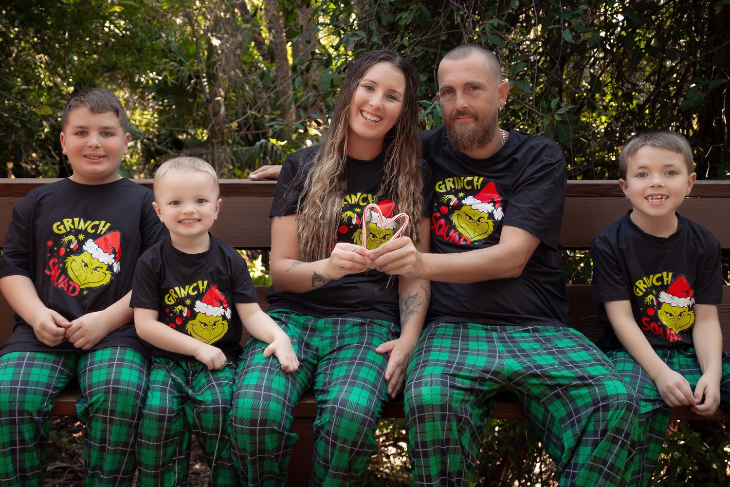Family of five in matching Grinch Christmas pajamas sitting on a bench outdoors.