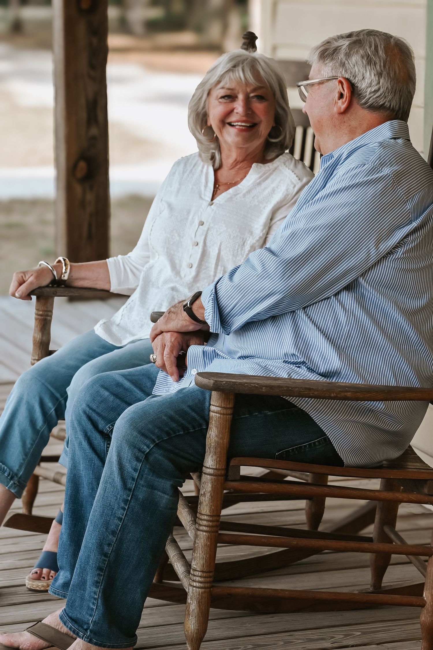 Happy senior couple laughing together while sitting in wooden rocking chairs on a porch.