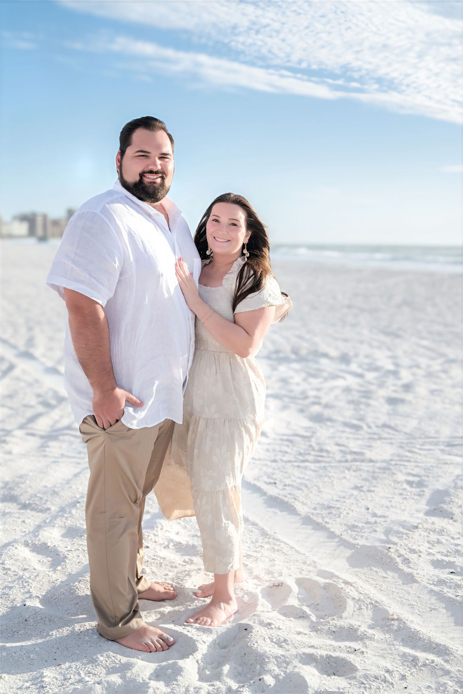 Smiling couple posing together on white sandy beach.