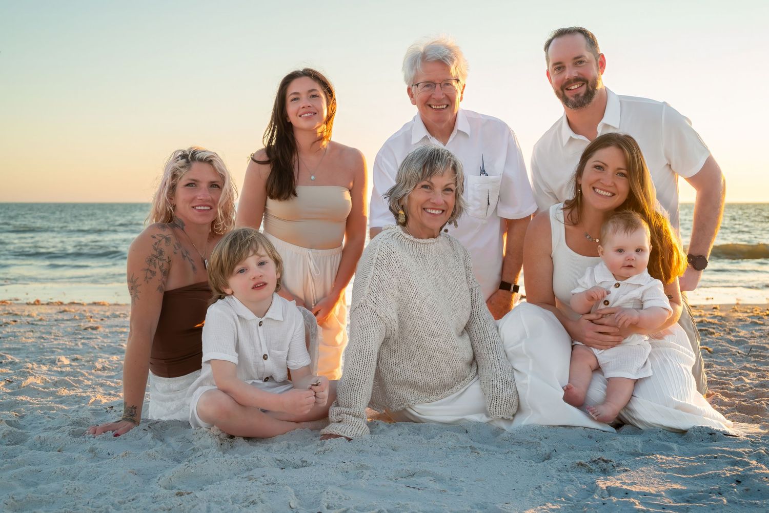 Multigenerational family portrait on beach at golden sunset with two young children and baby.