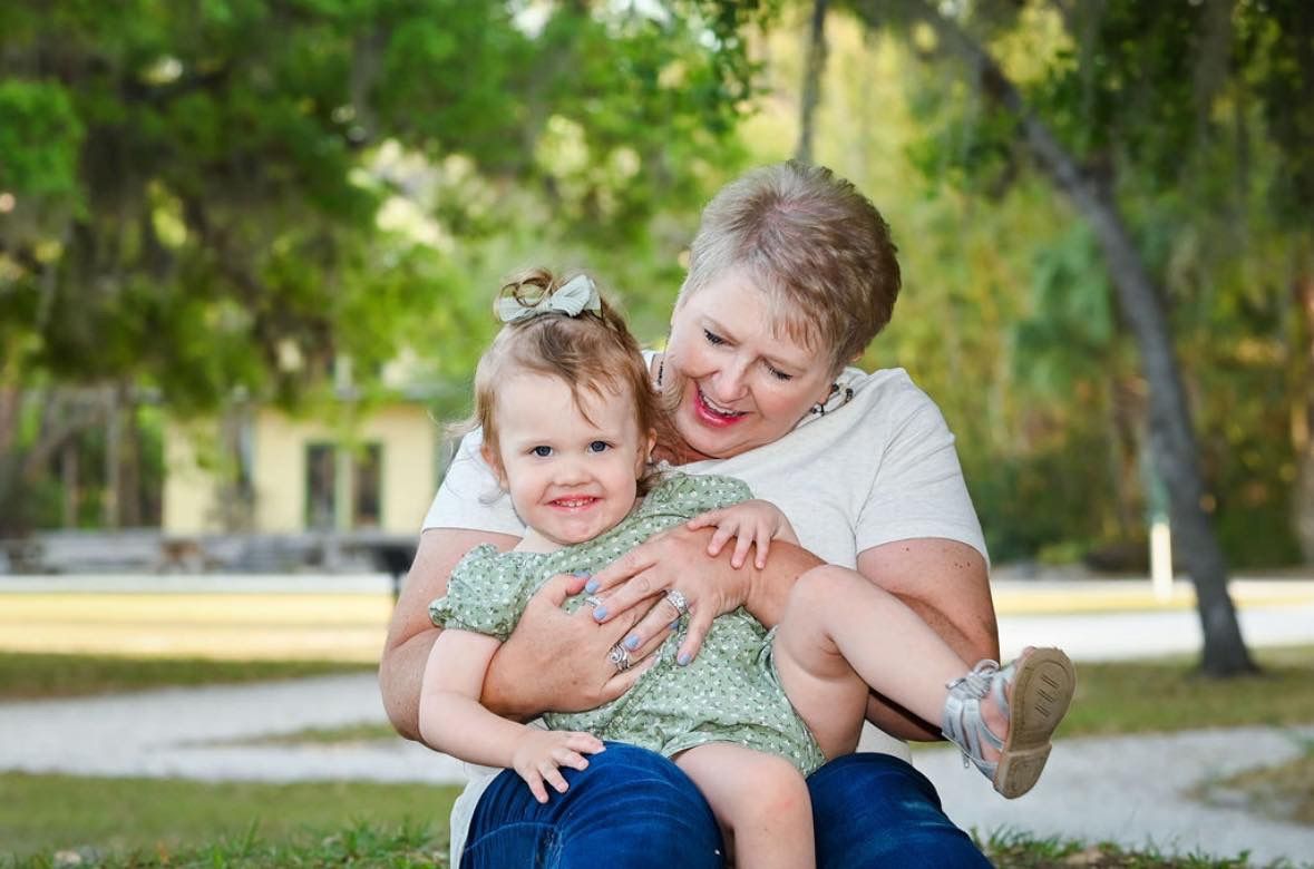 A grandmother smiling and hugging a happy toddler in a sunny park.