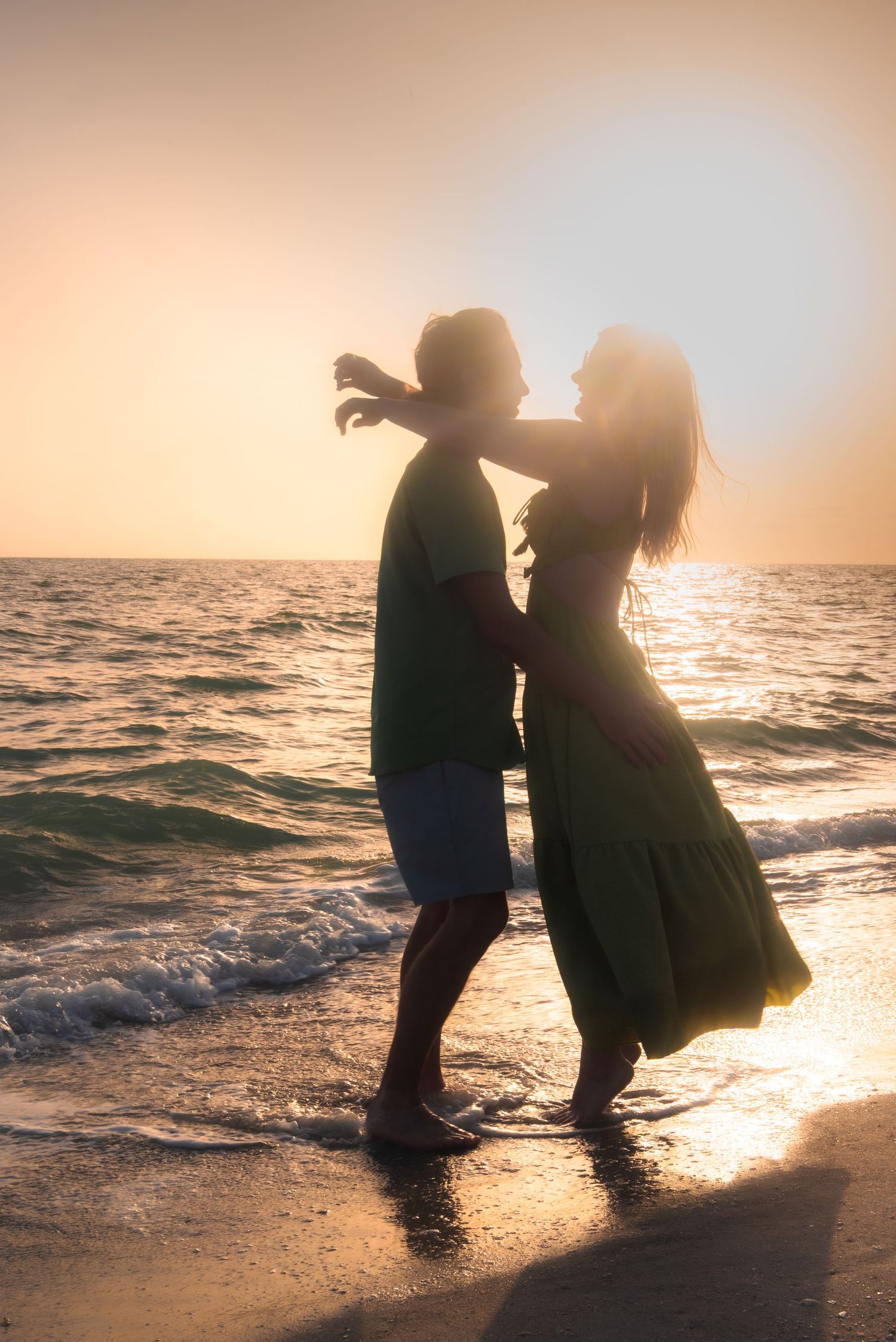 Romantic couple silhouetted against golden sunset on beach, dancing at the ocean shoreline.